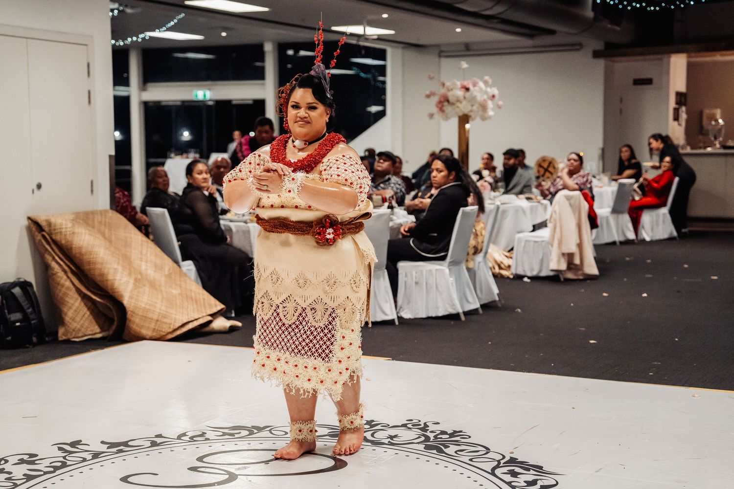 Wedding guest in traditional dress holds ceremonial items during indoor reception celebration.