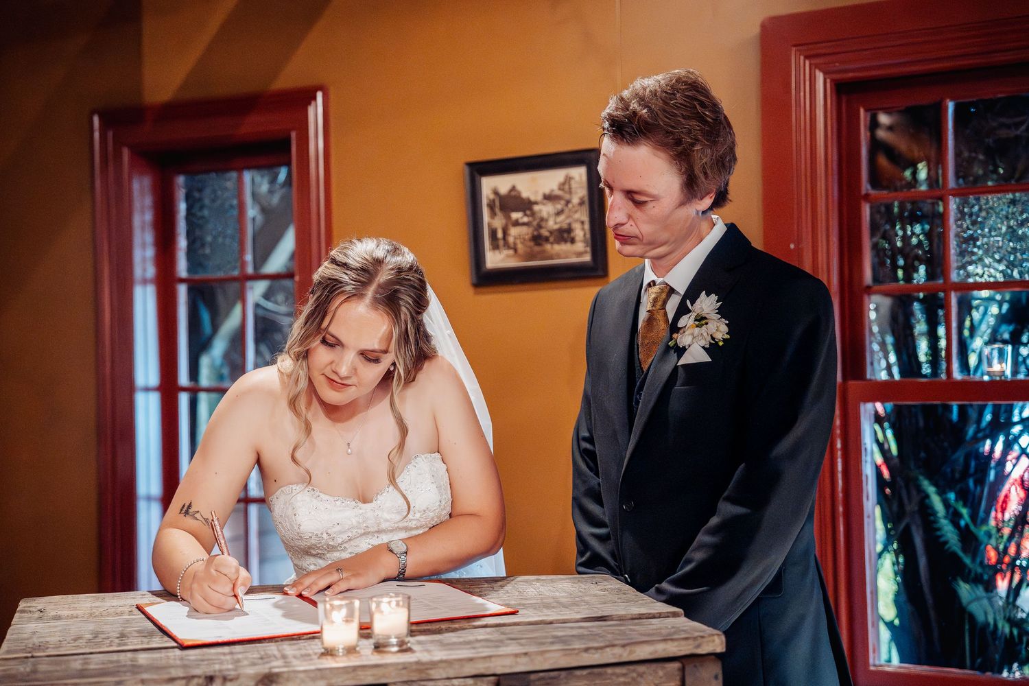 Happy couple completes marriage paperwork signing at rustic wooden table during wedding ceremony.