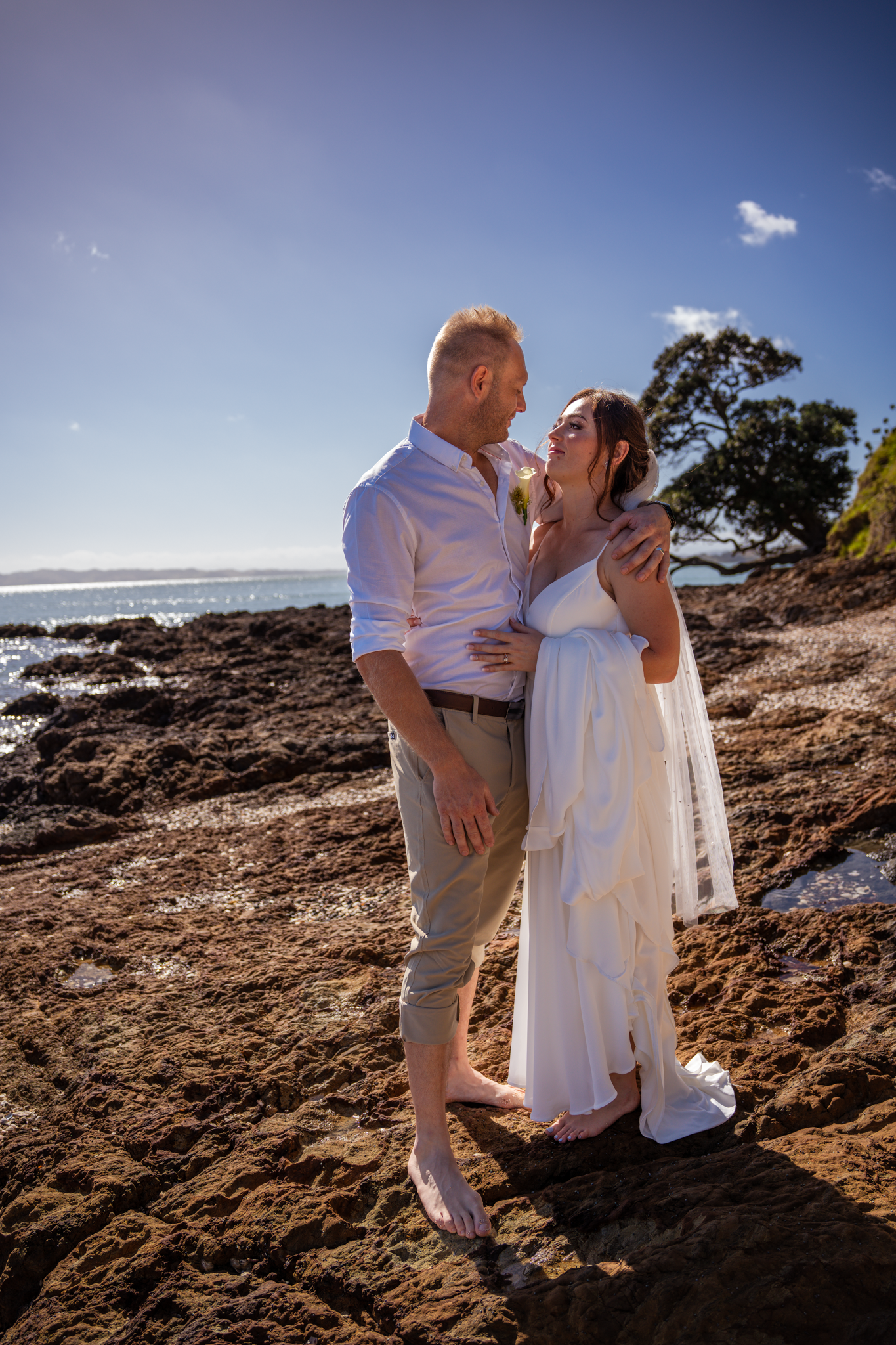 Wedding couple shares intimate moment on rocky beach landscape with ocean view.