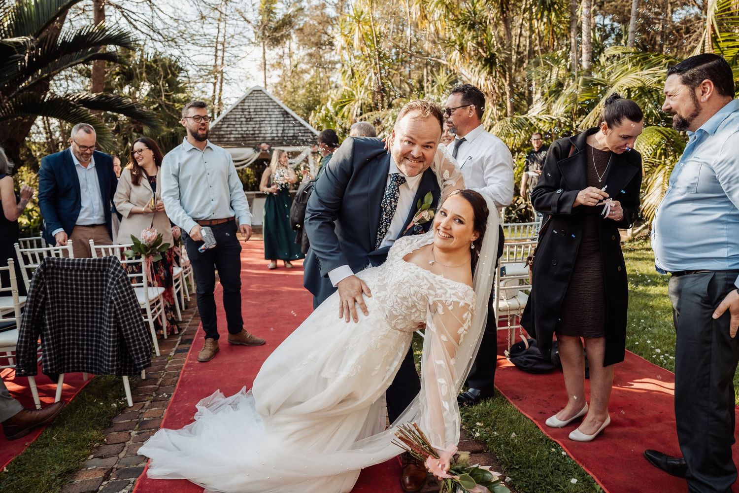 Wedding celebration on an outdoor red carpet with guests watching the festivities.