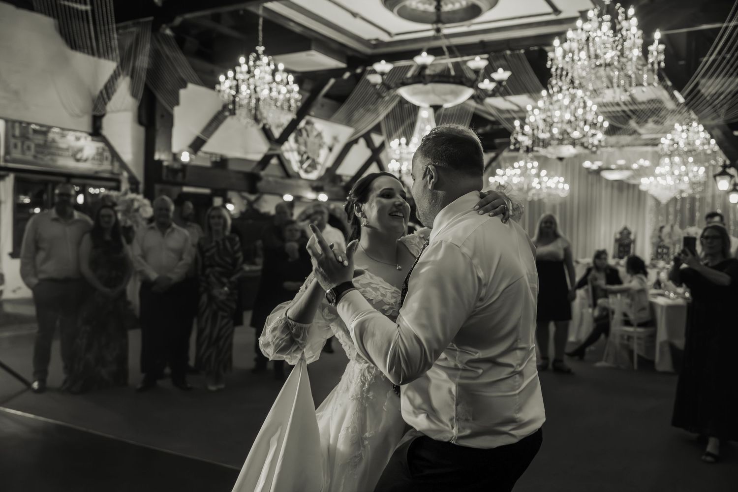 Black and white photo of wedding reception dance floor under crystal chandeliers.