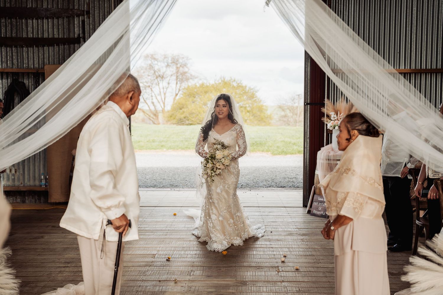 Wedding party celebrates in rustic barn venue with dramatic lighting and white decor.