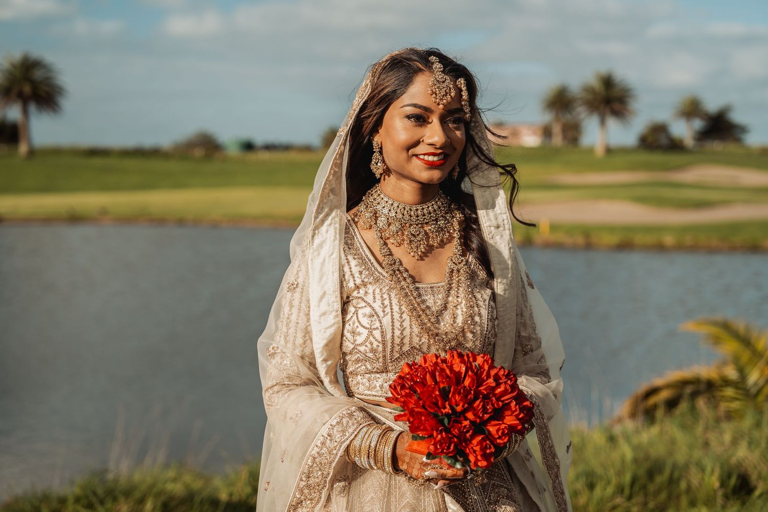 Wedding photoshoot by waterfront with palm trees and lush greenery in background.