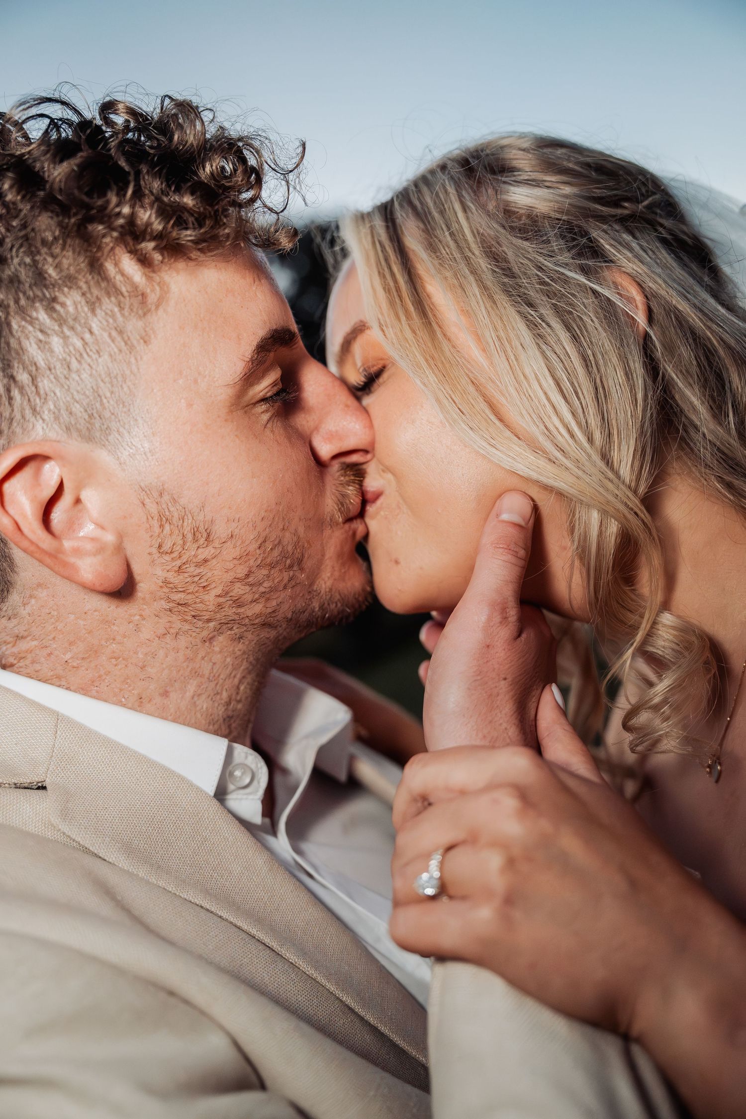 Close-up of newlyweds sharing a romantic kiss with bride's diamond engagement ring visible.