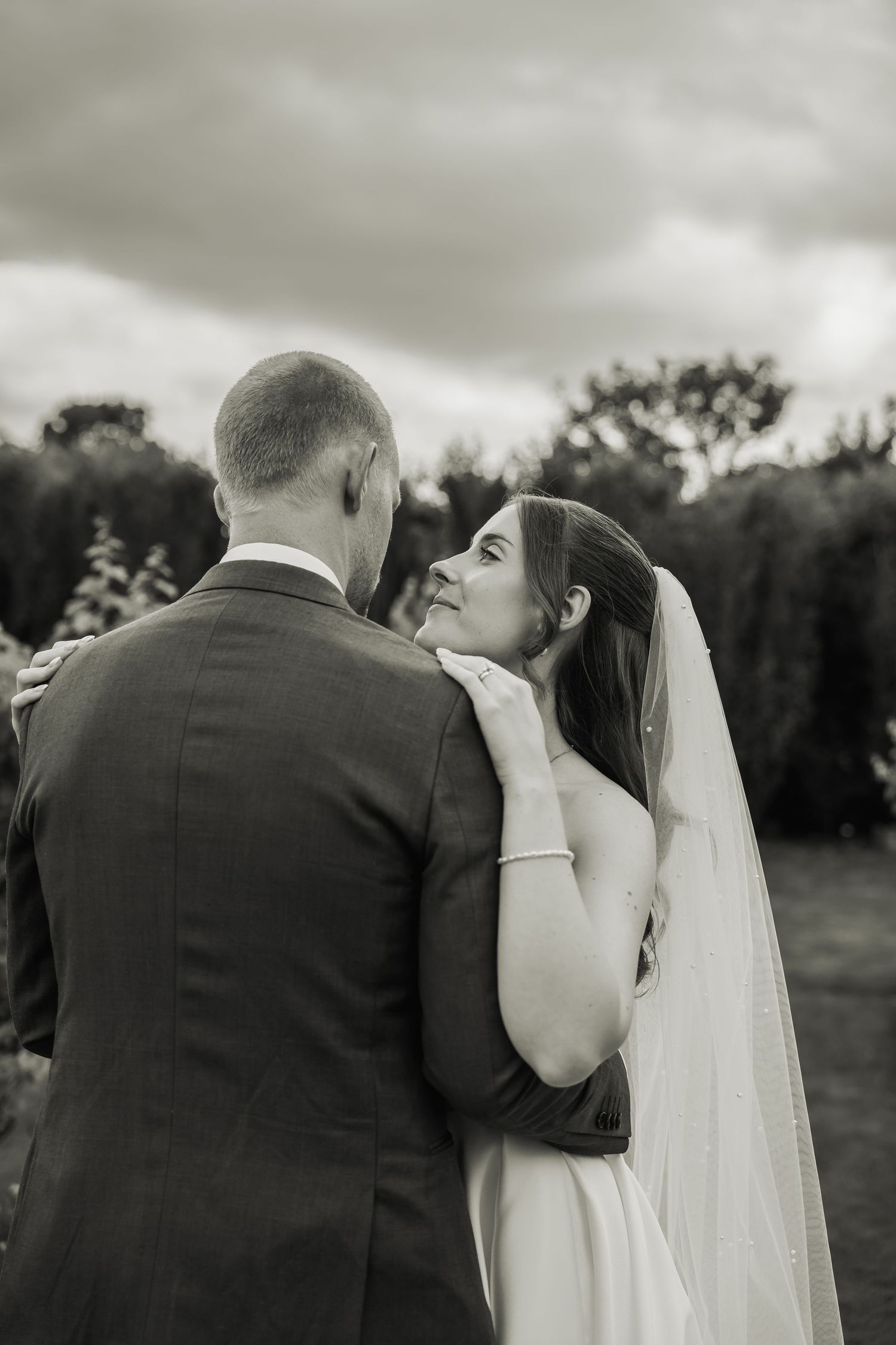 Black and white portrait of a bride gazing lovingly at her groom during an outdoor wedding ceremony.