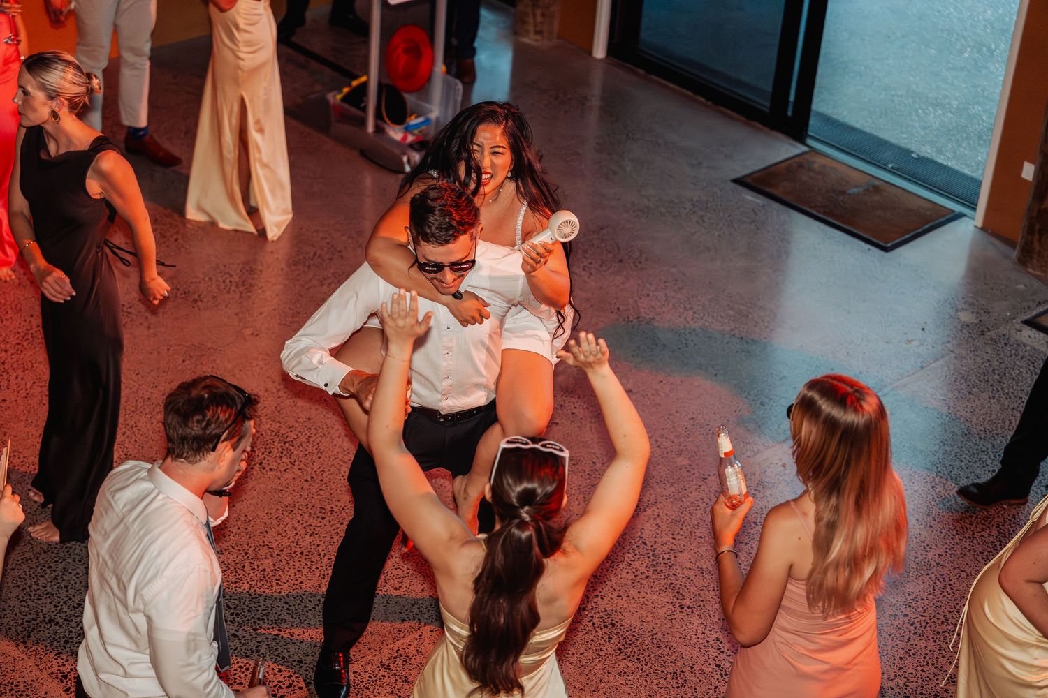 Guests dancing and celebrating at a lively wedding reception with colorful lighting.