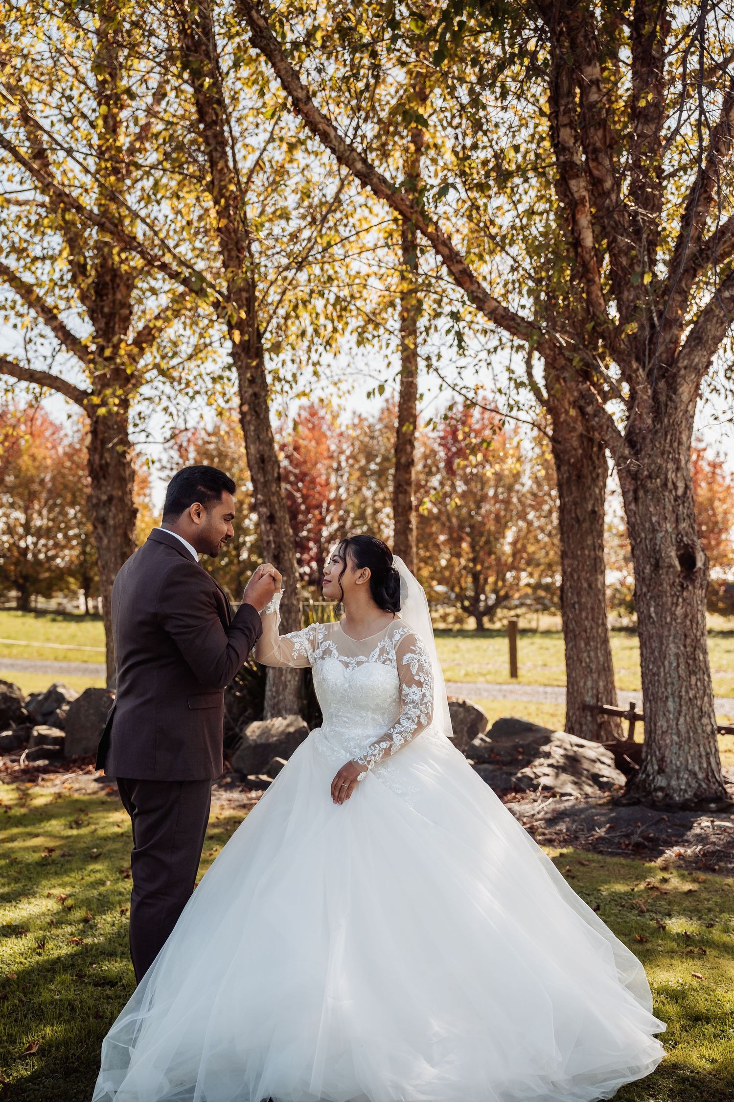 Bride and groom share romantic moment holding hands among colorful autumn trees in park setting.