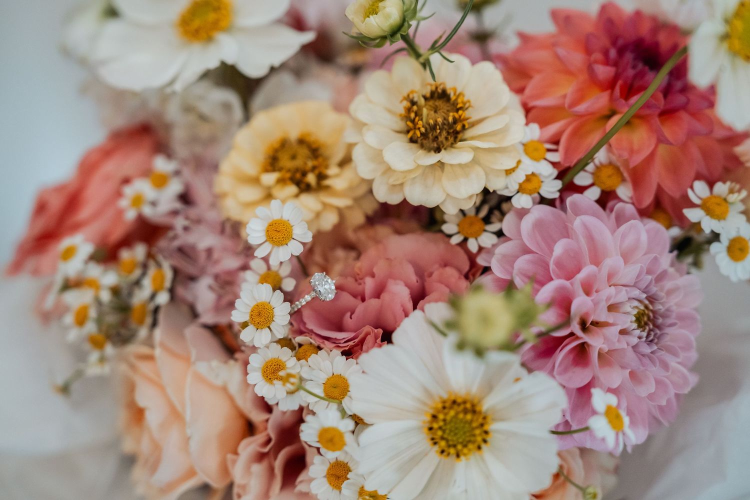 A beautiful bouquet of mixed flowers including pink dahlias, white daisies, and peach roses for a wedding.