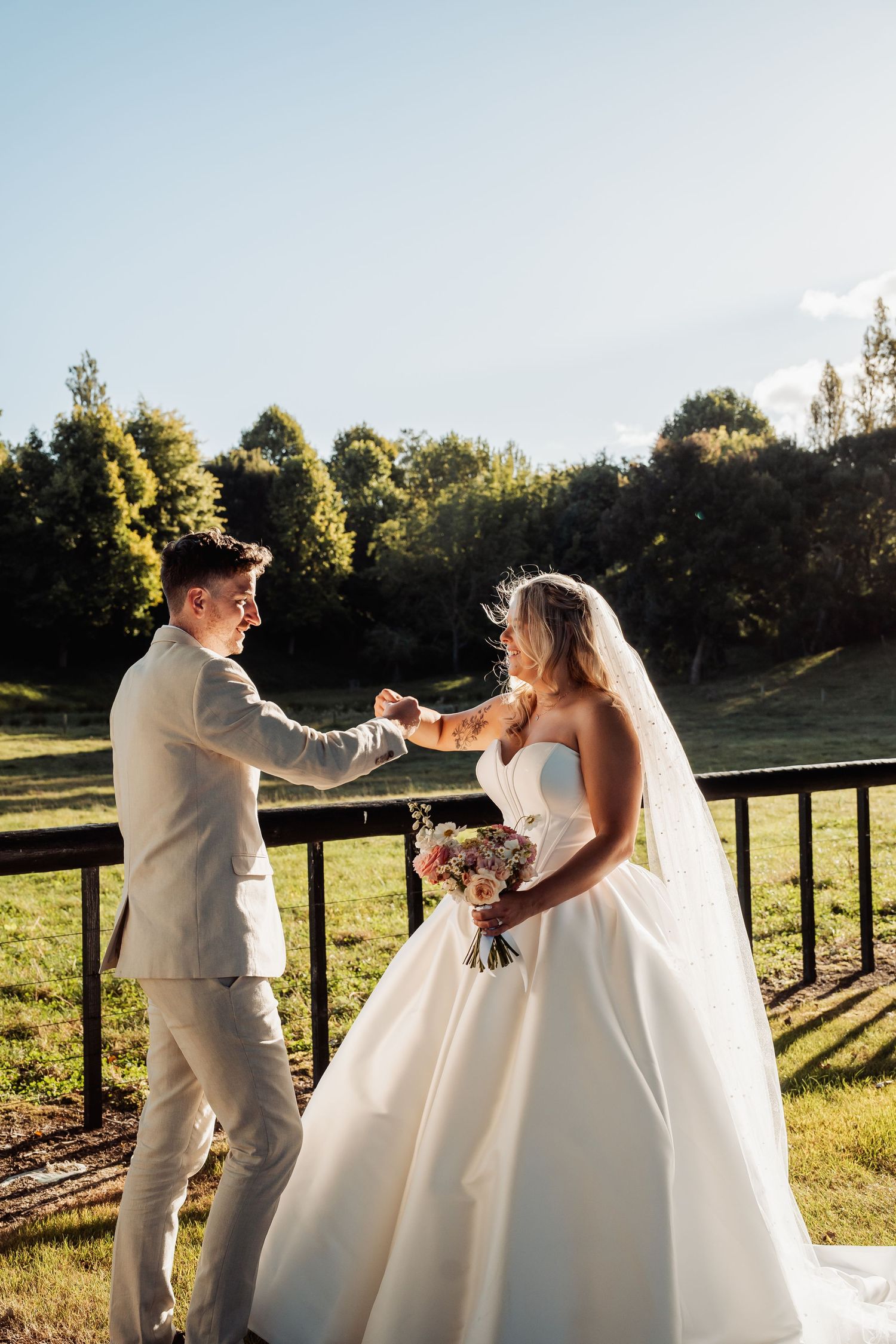 Bride and groom holding hands on a sunny day with green countryside in the background.