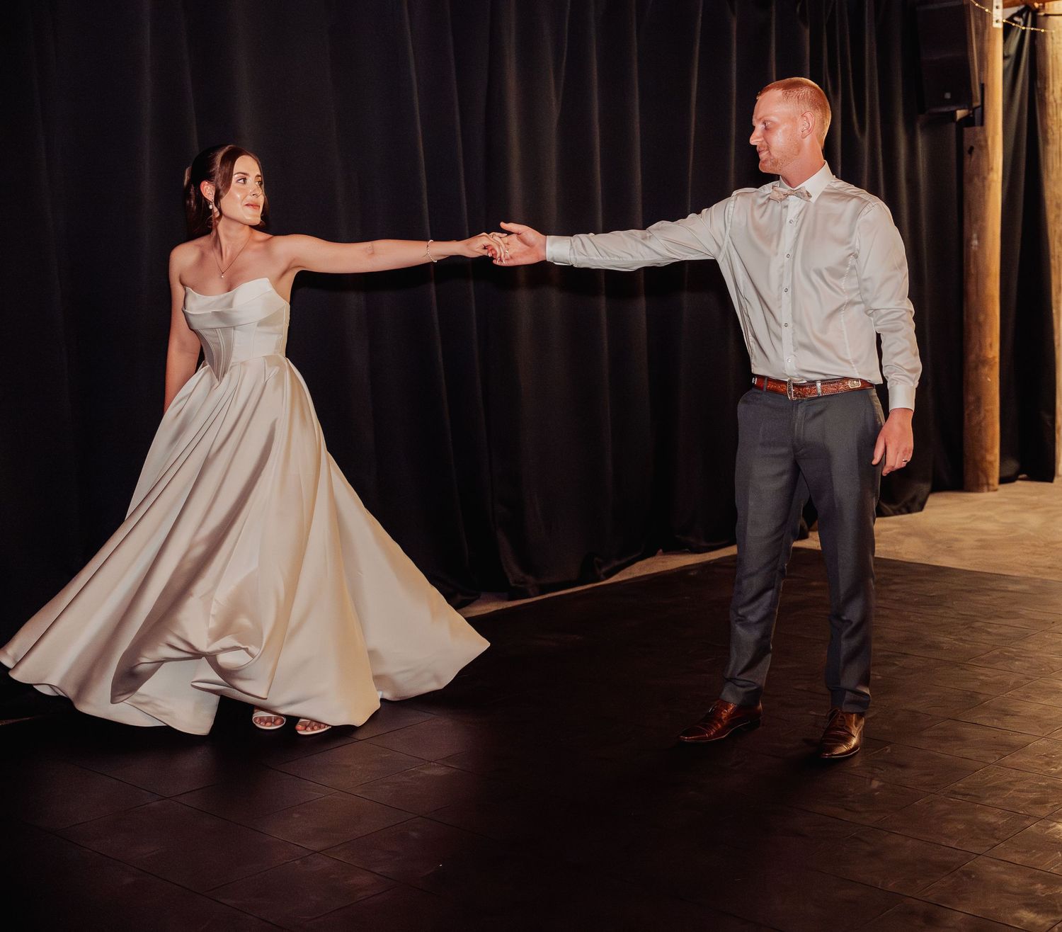 Bride and groom share a romantic first dance, with the bride's satin gown flowing as they spin on a darkened dance floor.