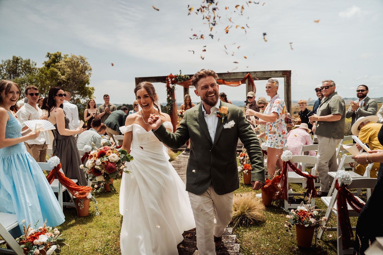 Newlywed couple walking back down aisle as guests throw confetti at outdoor wedding celebration.