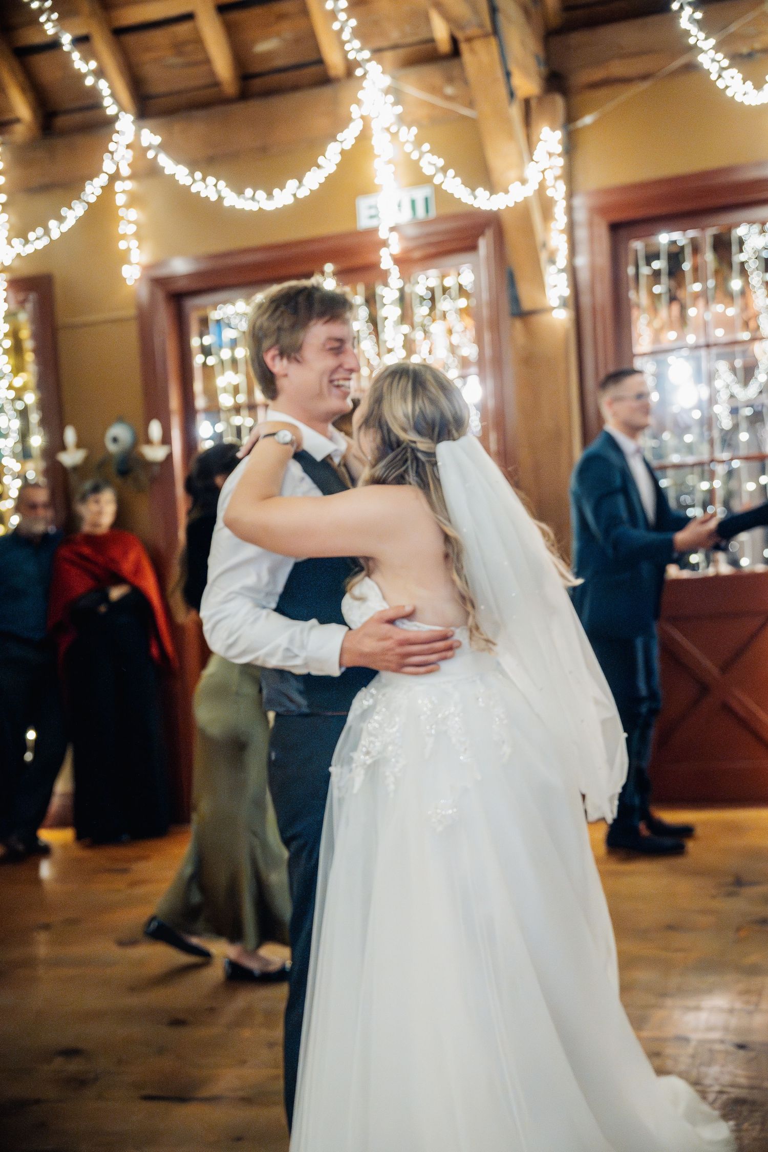 Romantic first dance under twinkling string lights at indoor wedding reception.