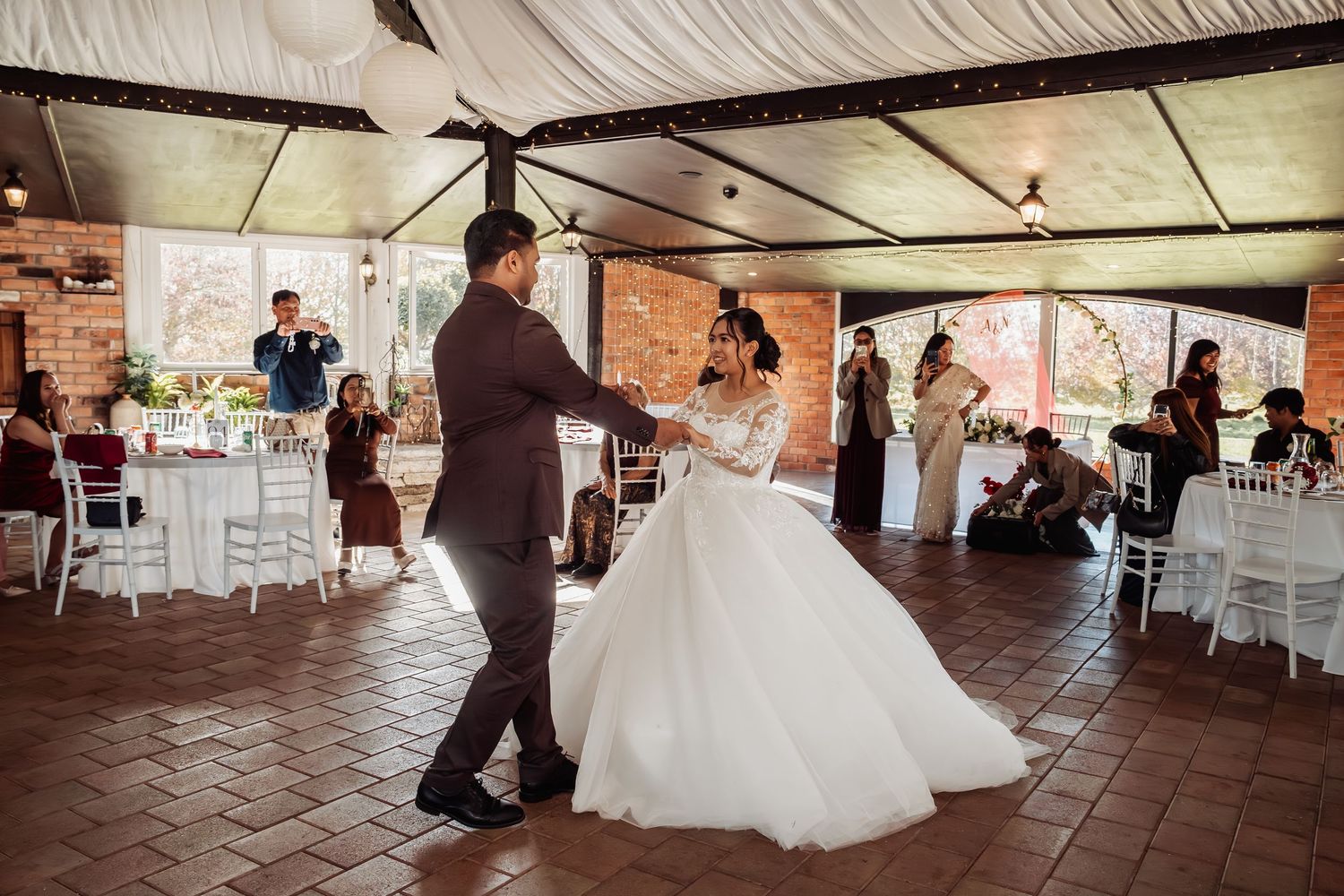 Bride and groom share their first dance at an elegant outdoor wedding reception with guests watching.