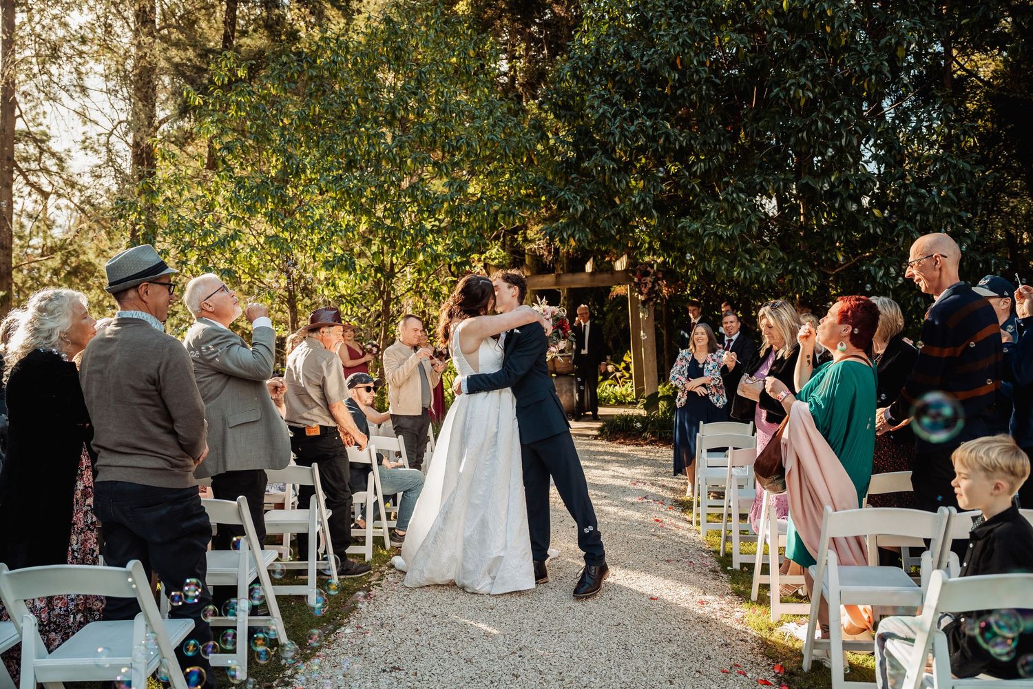 Bride and groom share first dance on outdoor wedding aisle with guests celebrating.