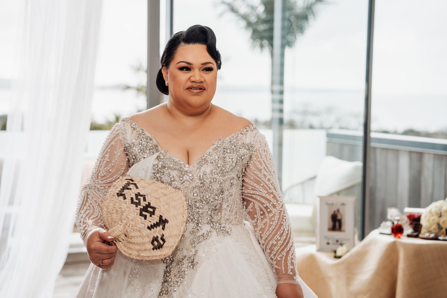 A bride in a white lace wedding gown poses at a windowed venue on her special day.