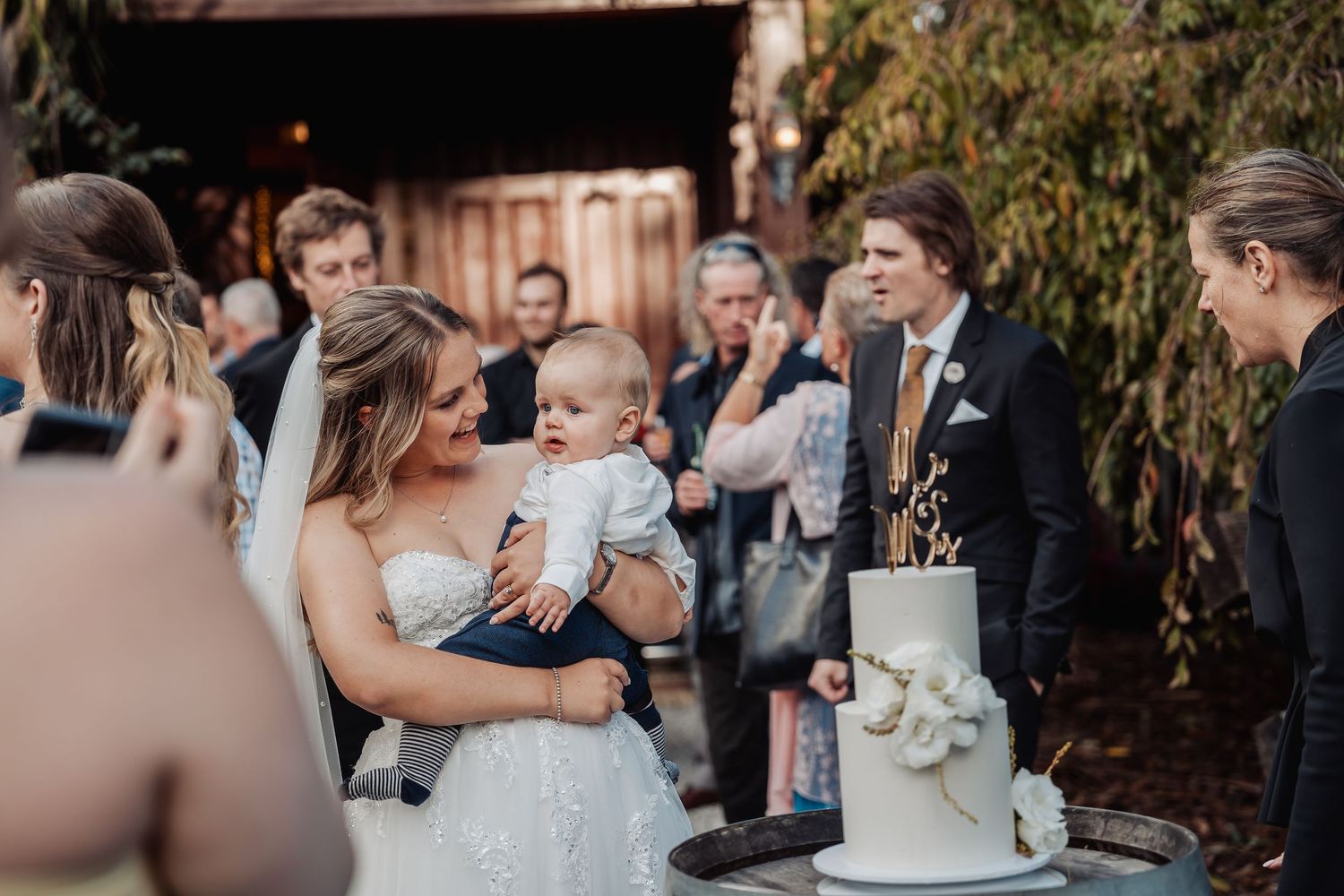 Elegant outdoor wedding reception with wedding cake and guests gathered around during intimate celebration moment.