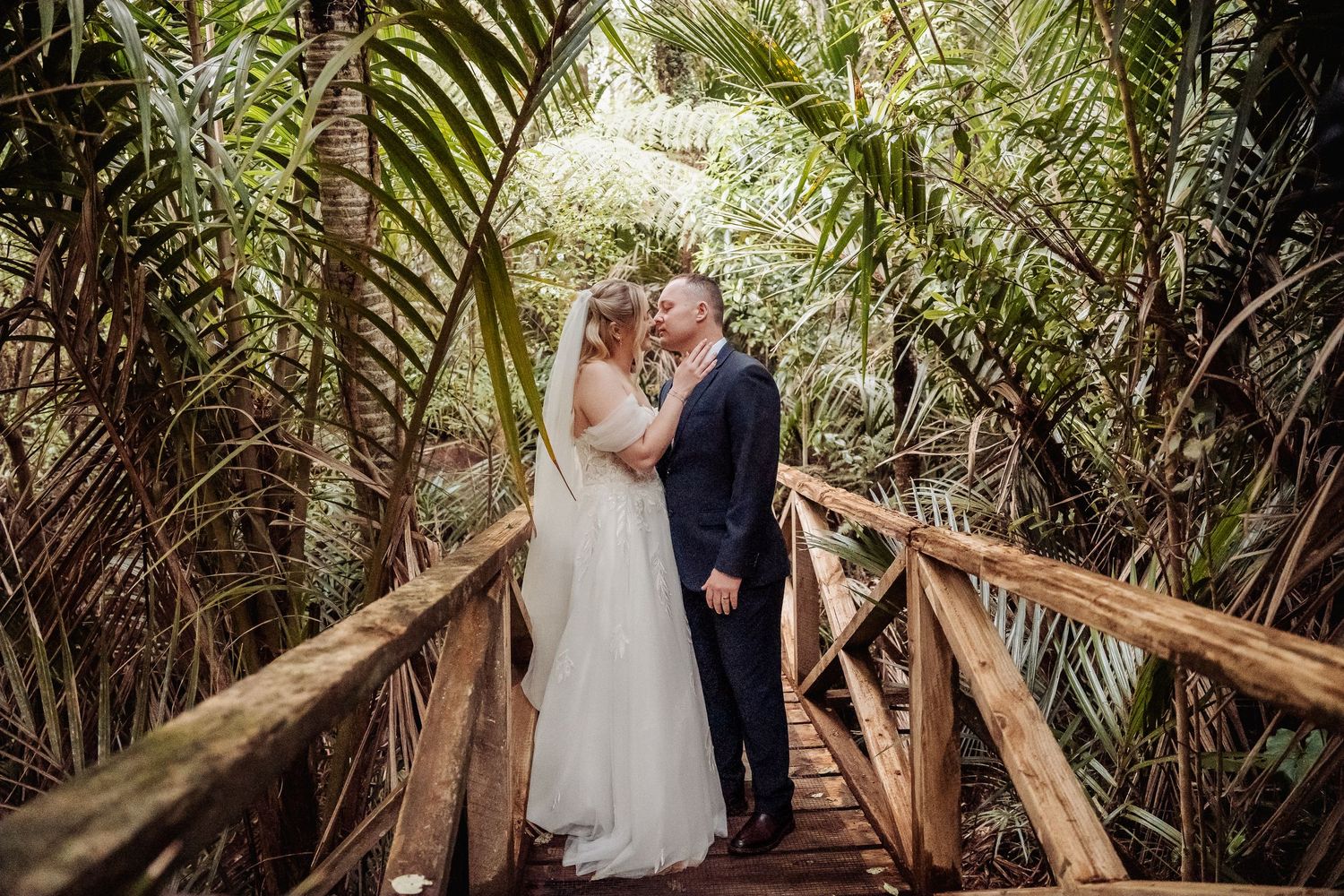 A romantic moment on a wooden bridge surrounded by tropical palm fronds.