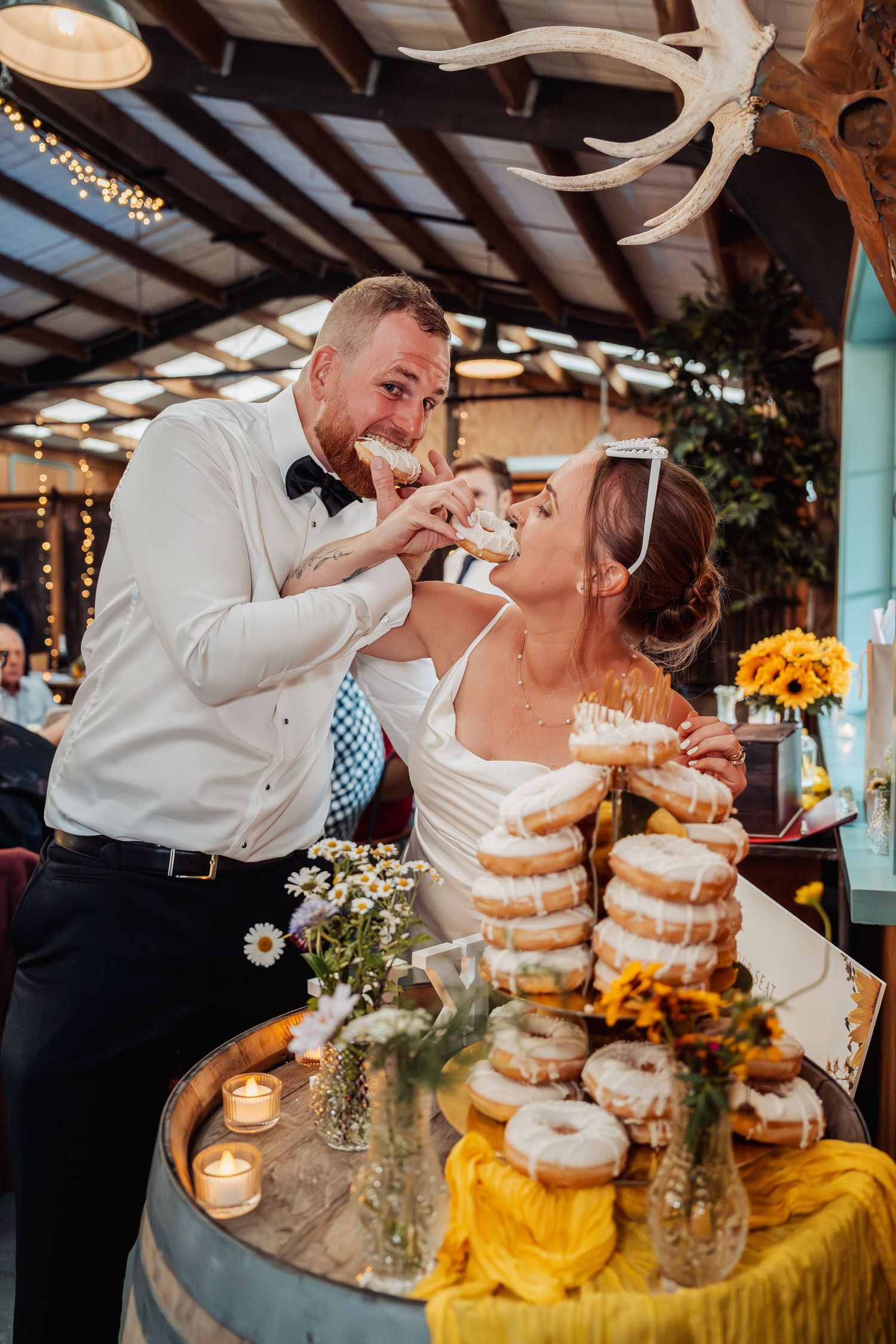 Bride and groom feed each other donuts from a rustic barrel display at their wedding reception.
