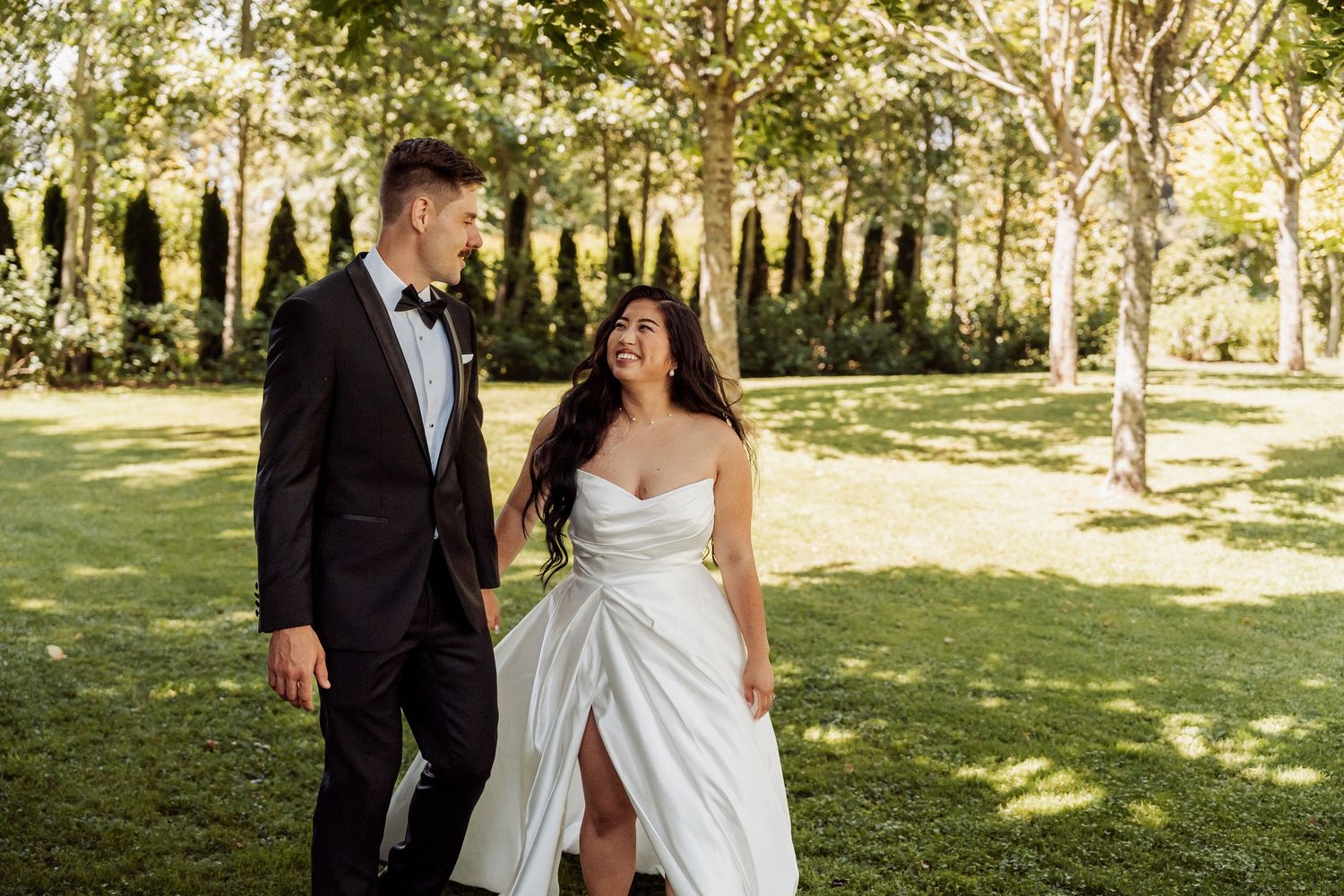 A bride and groom walk hand in hand through a lush green garden on their wedding day.