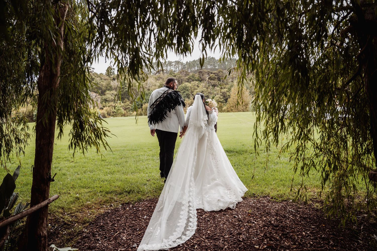Newlywed couple walks hand in hand through a scenic green garden after their wedding.