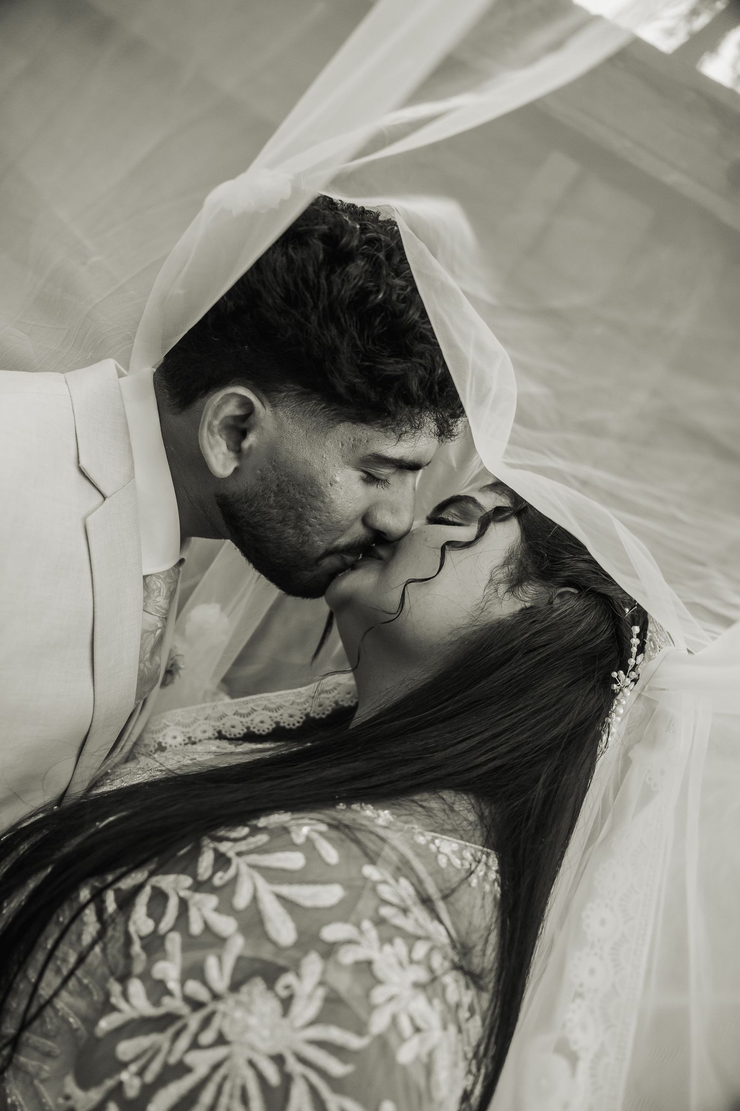 Romantic black and white photo of bride and groom kissing beneath flowing wedding veil.