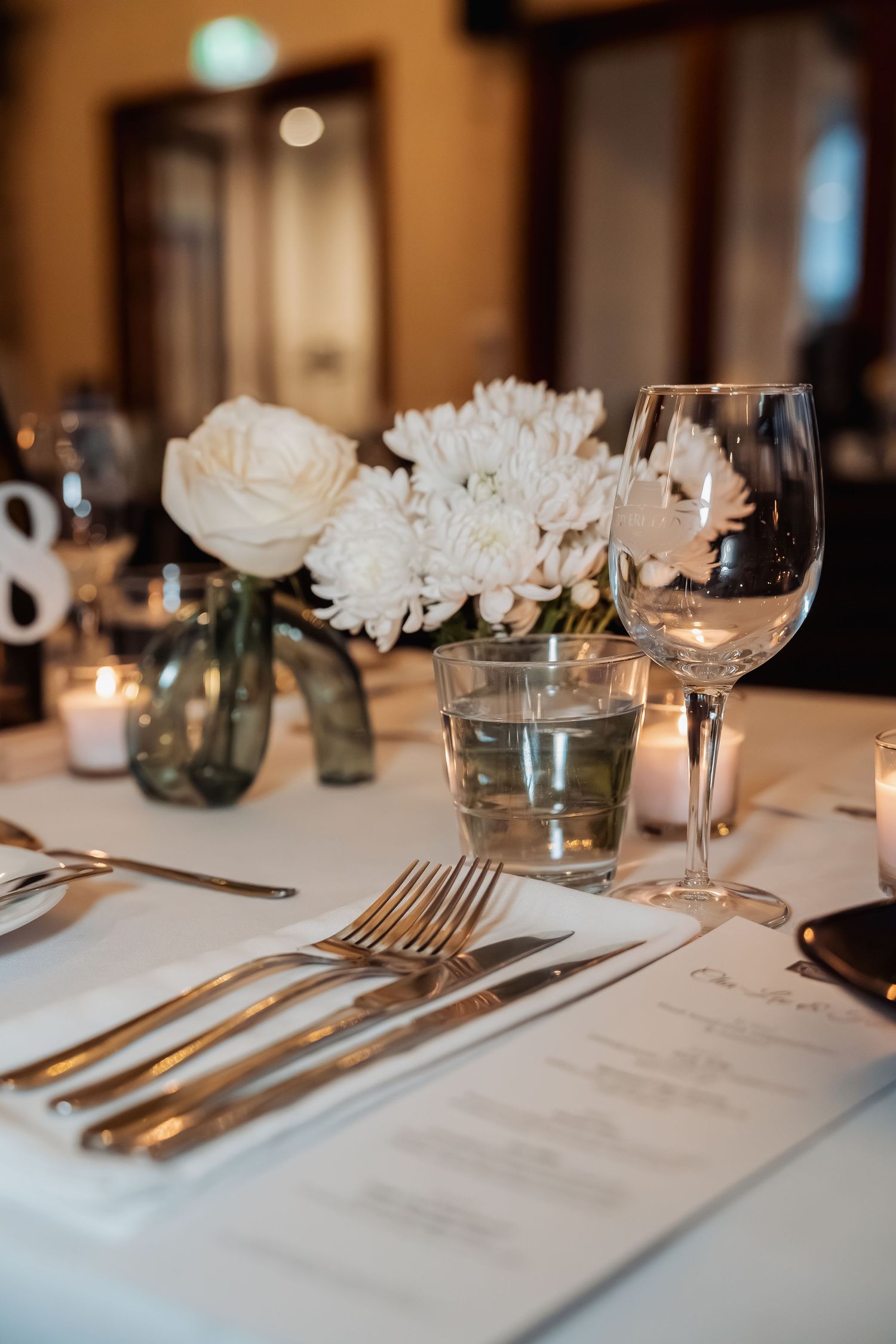 Elegant table setting with white flowers, wine glasses and silverware on crisp white linen for upscale dining.