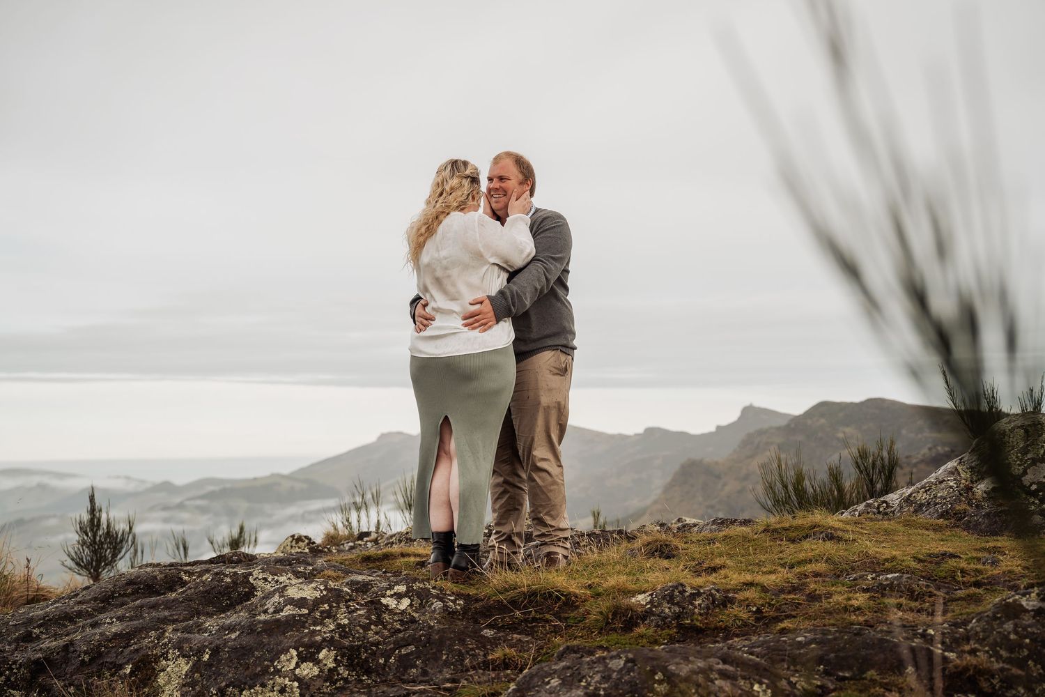 A couple embraces on a misty cliff overlooking the ocean on a moody Pacific Northwest coastline.