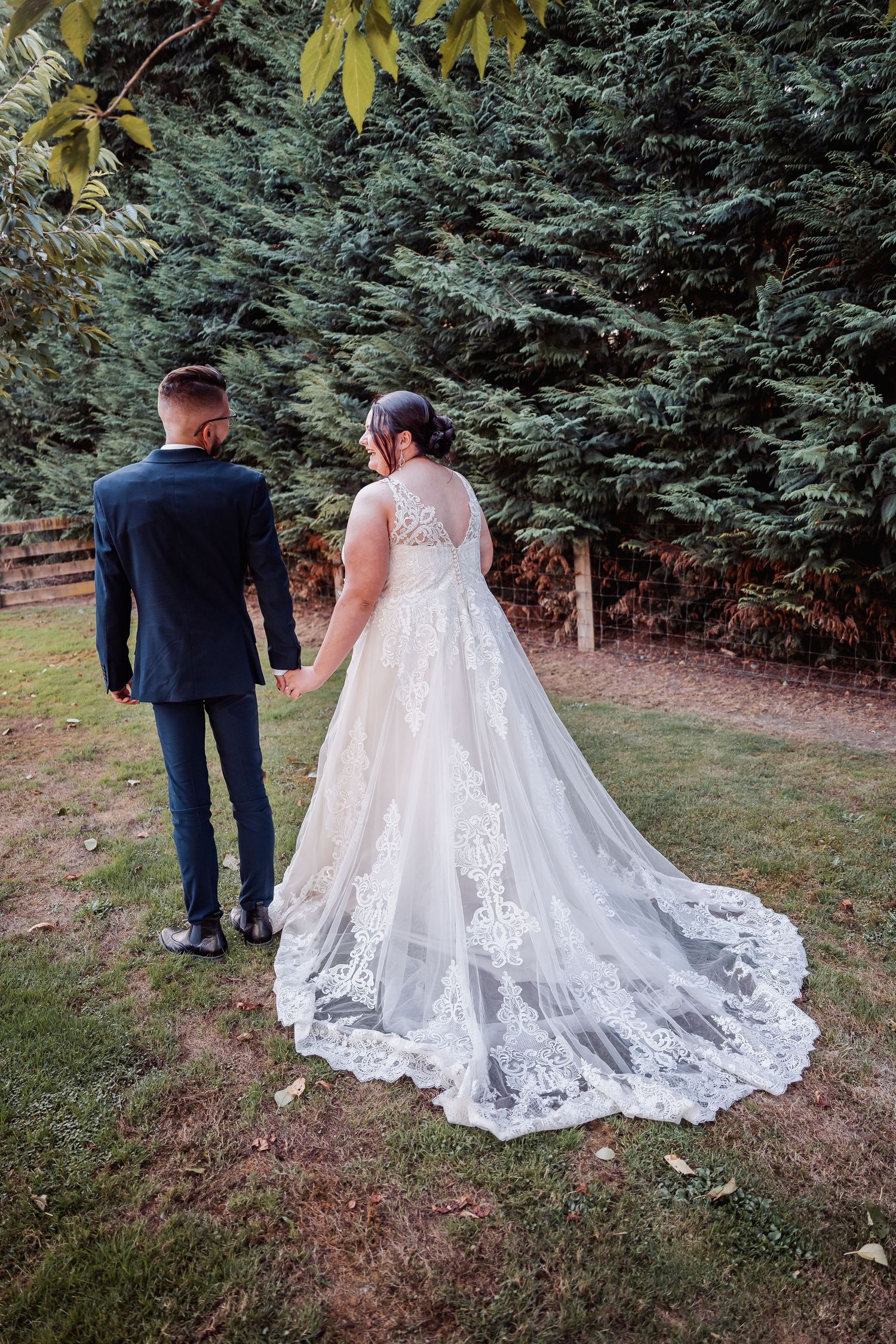 Newlyweds walking together on a garden path with the bride wearing a stunning lace train wedding dress.