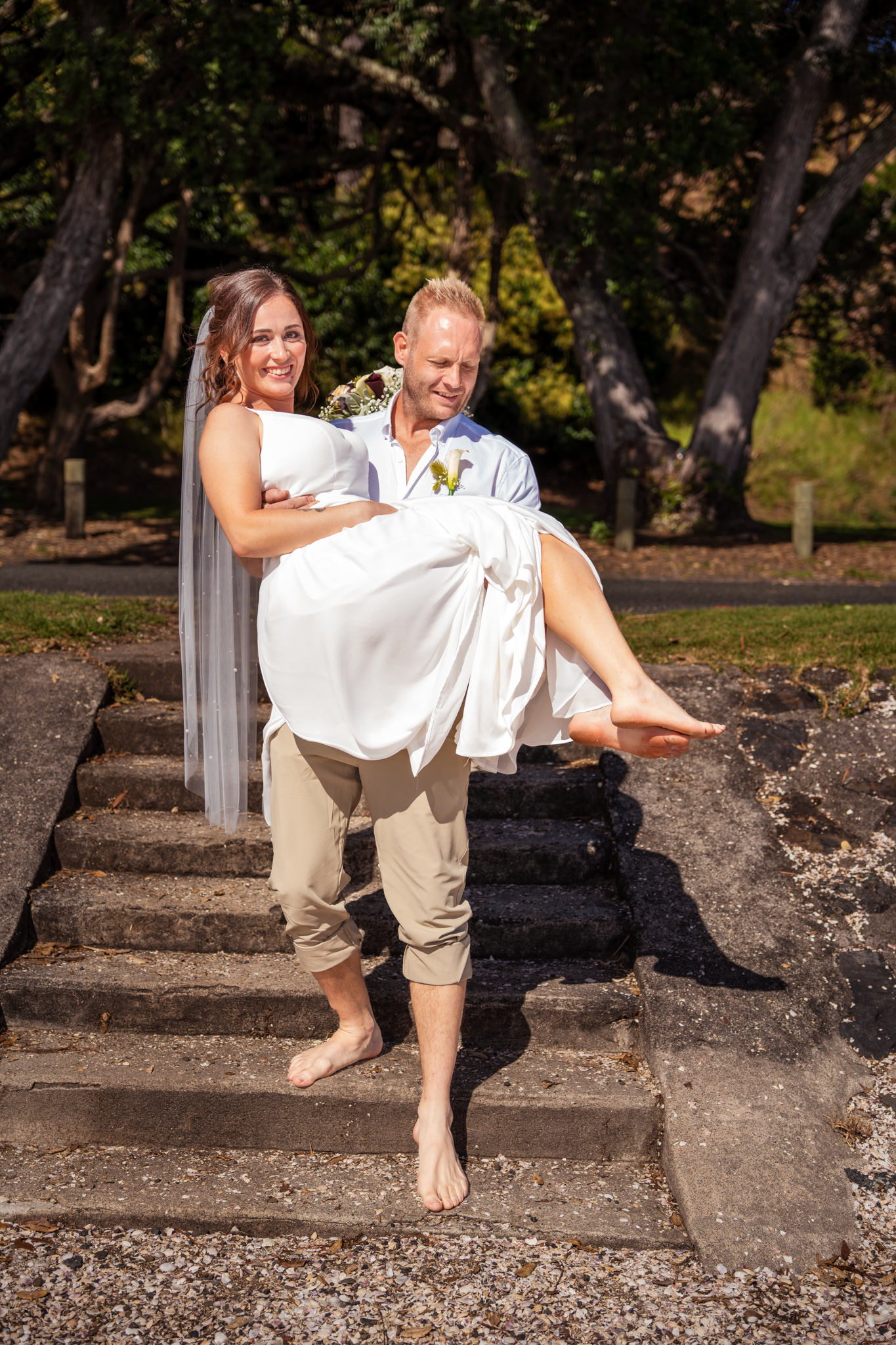 A couple in wedding attire poses on stone steps in a garden setting.