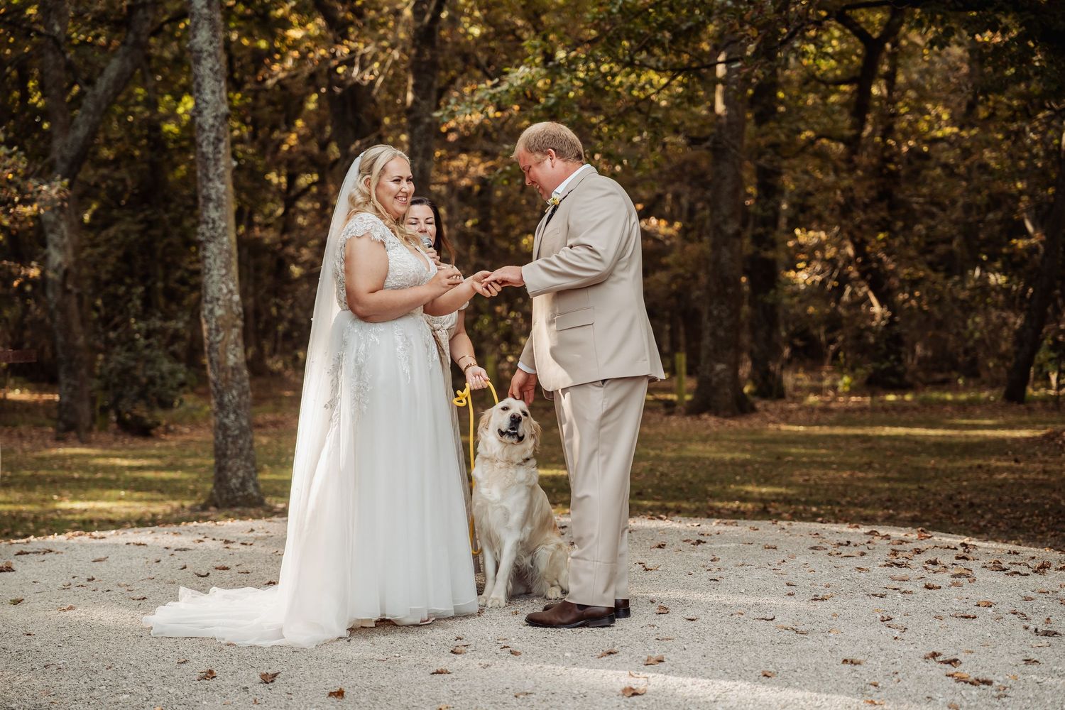 Bride and groom exchanging rings with golden retriever dog at outdoor ceremony.