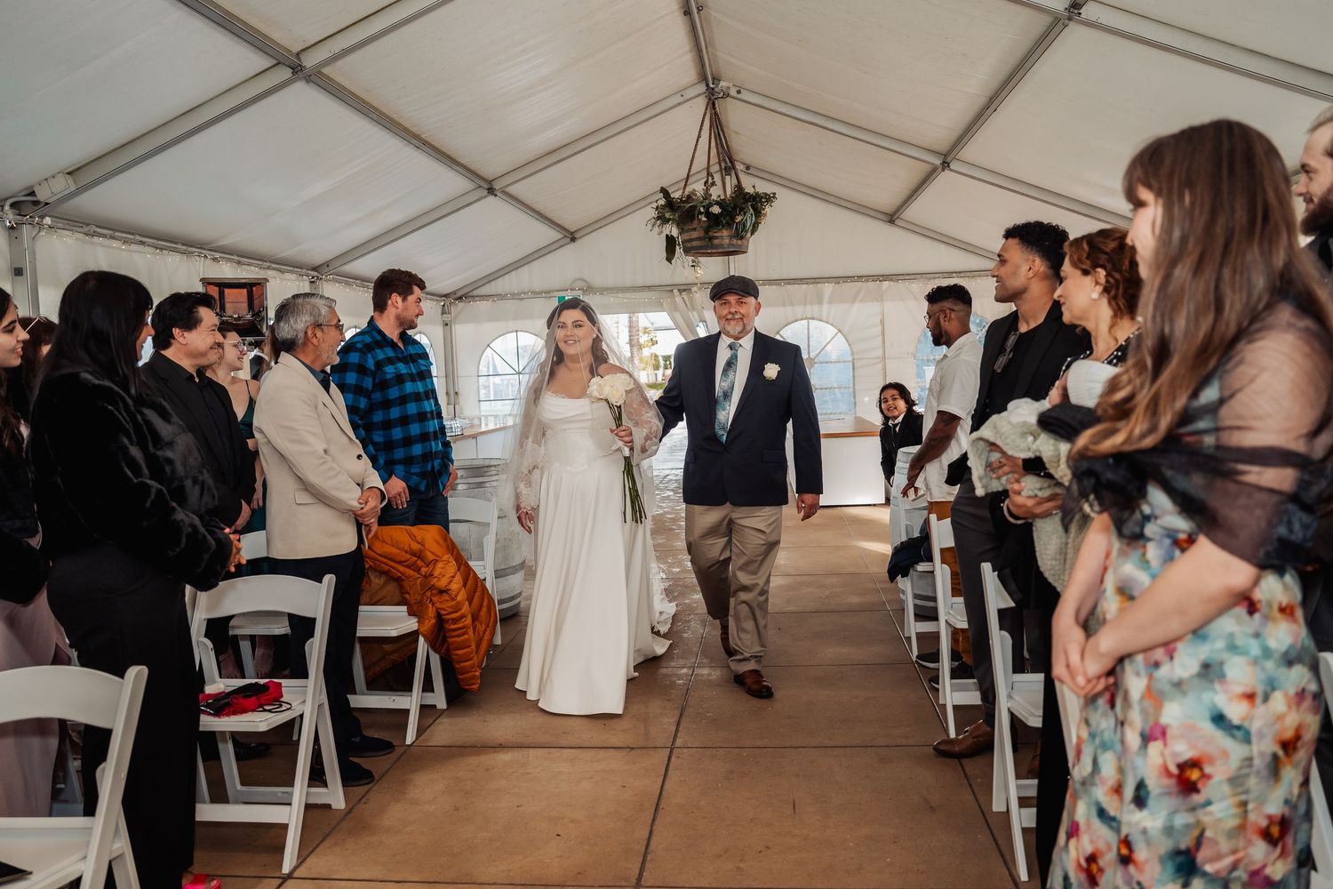 Wedding ceremony in a white tent with guests lining the aisle as couple walks down during recessional.