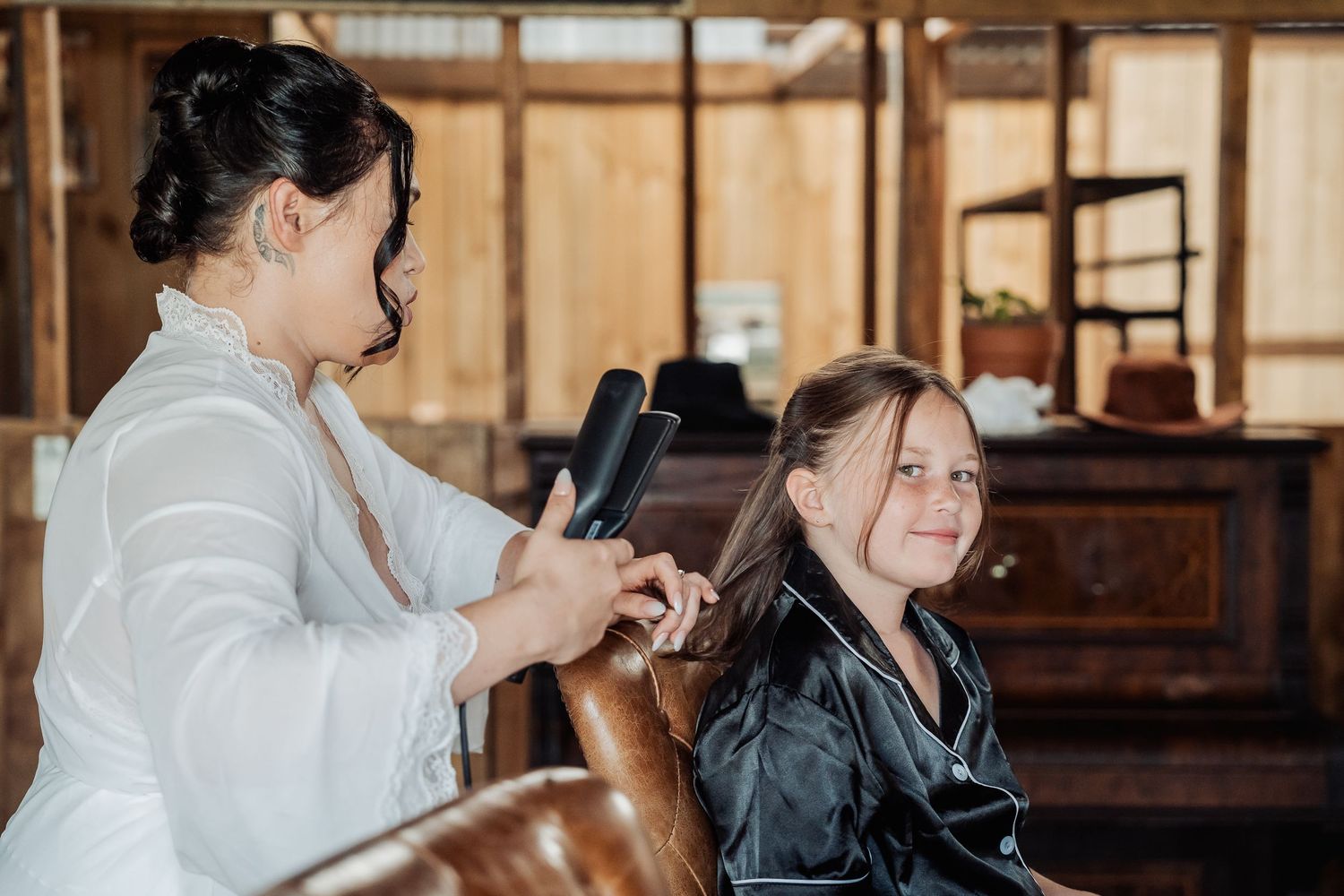 A stylist works on a client's hair in a rustic salon setting with wooden walls and vintage furniture.