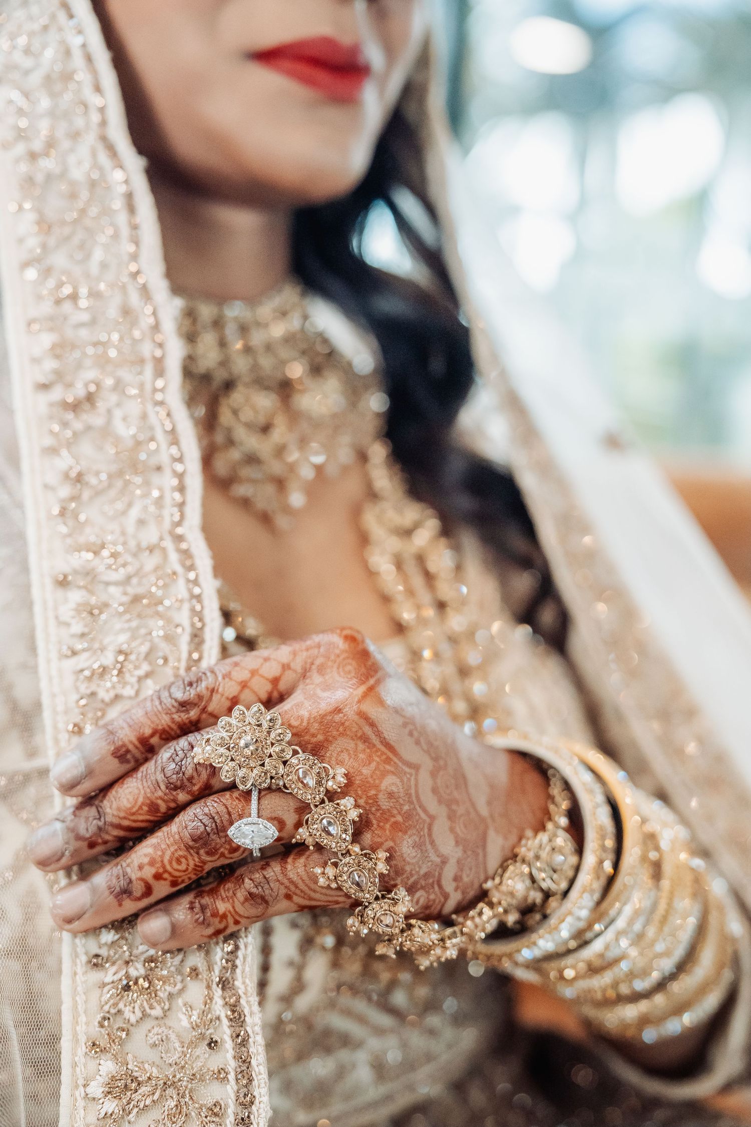 Close-up of intricate bridal jewelry and henna-decorated hands with bangles and rings.