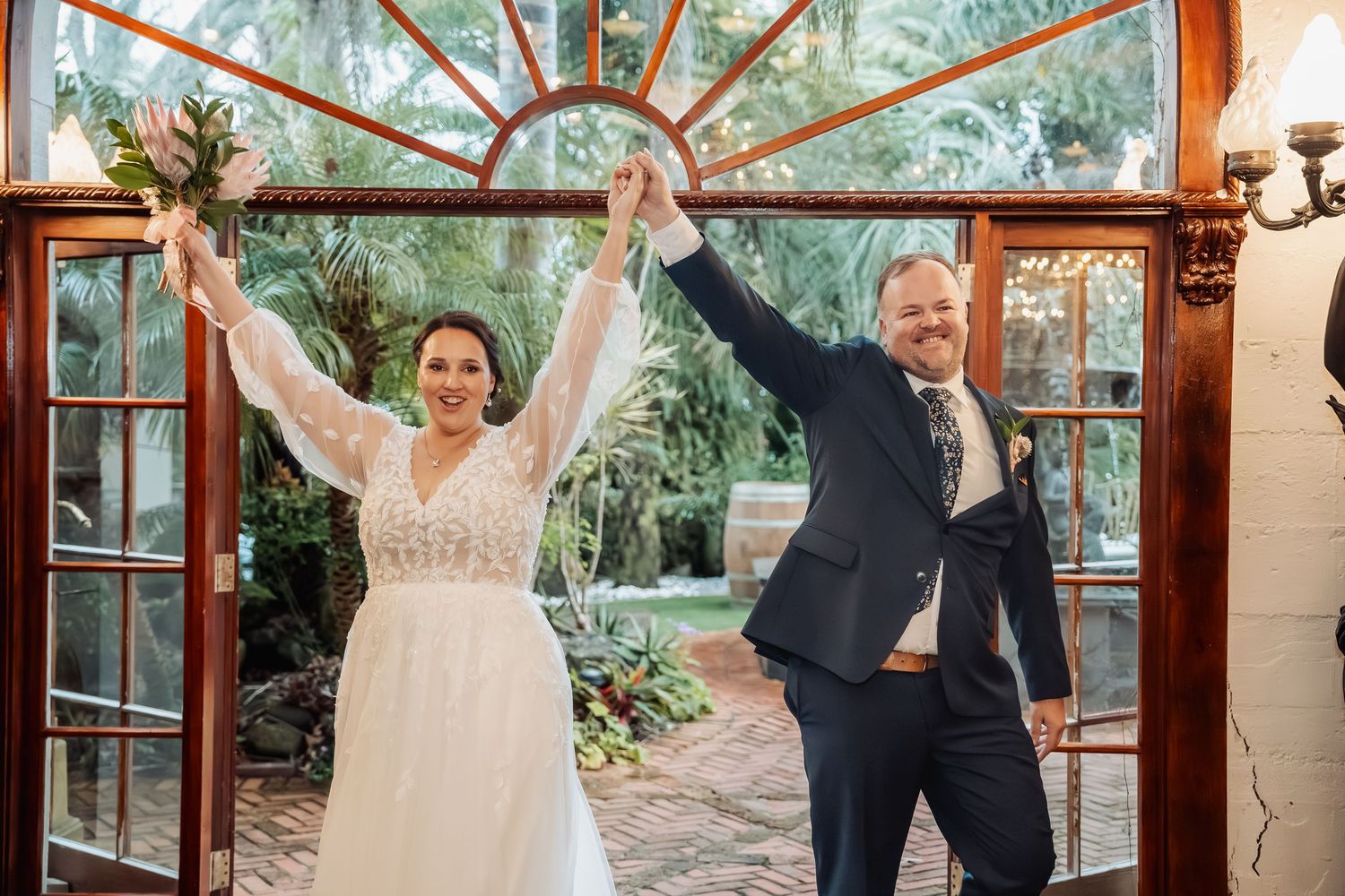 Couple shares playful dance moves in a rustic conservatory with wood and glass architecture.