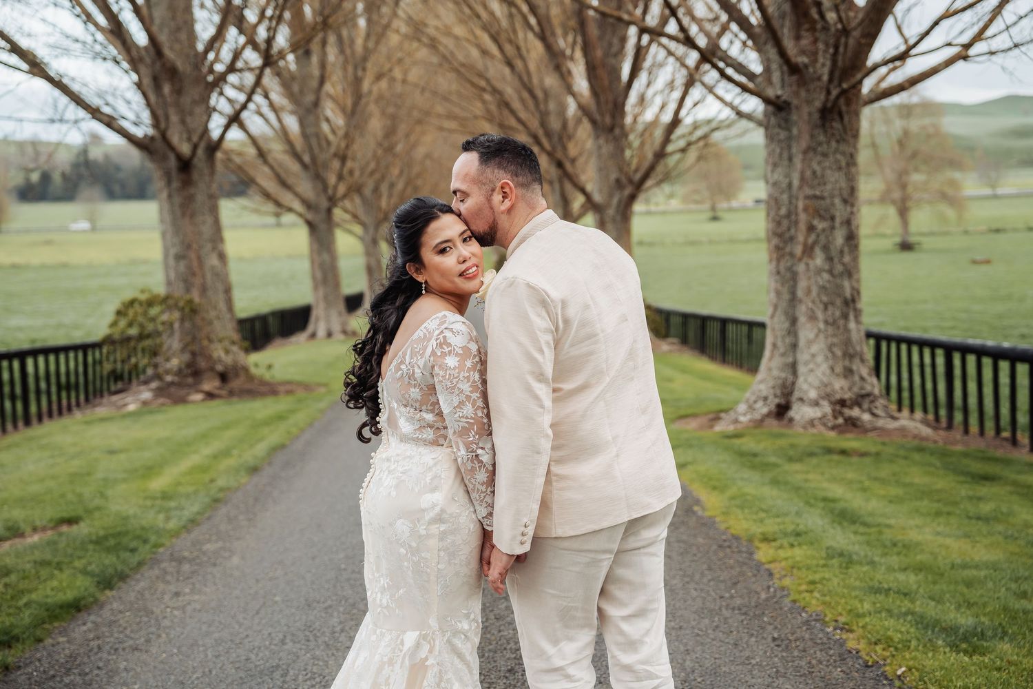 Newlyweds share romantic moments on a tree-lined country path.