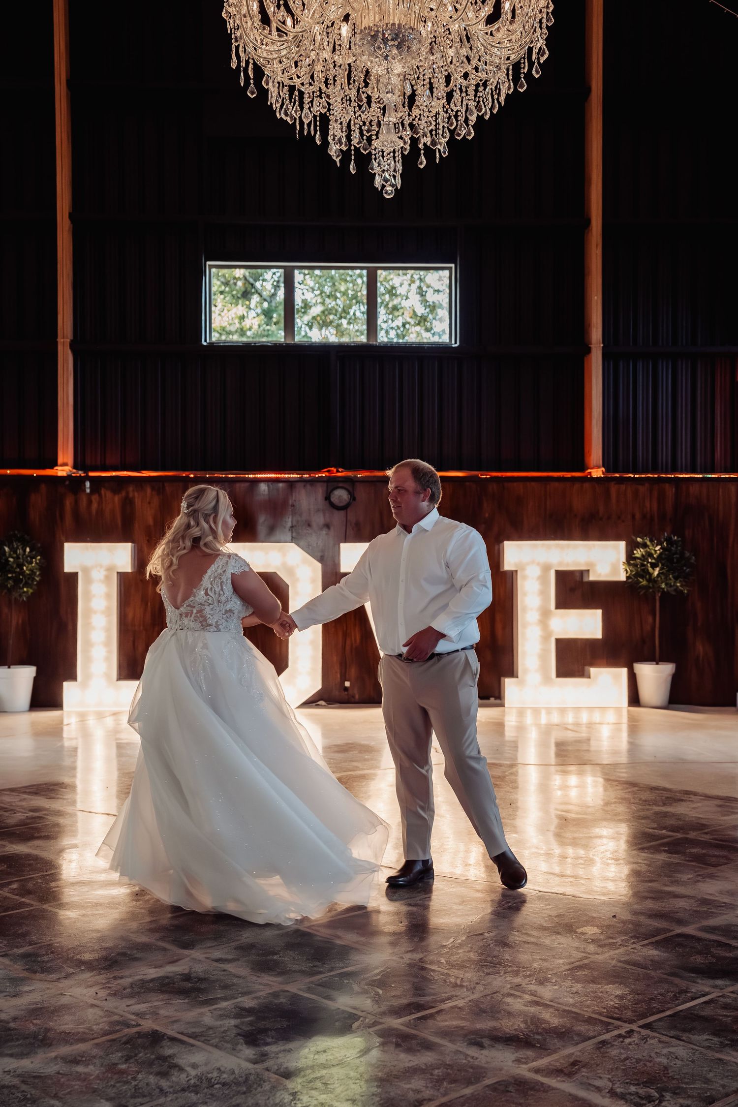 Bride and groom share first dance under crystal chandelier with illuminated LOVE letters.