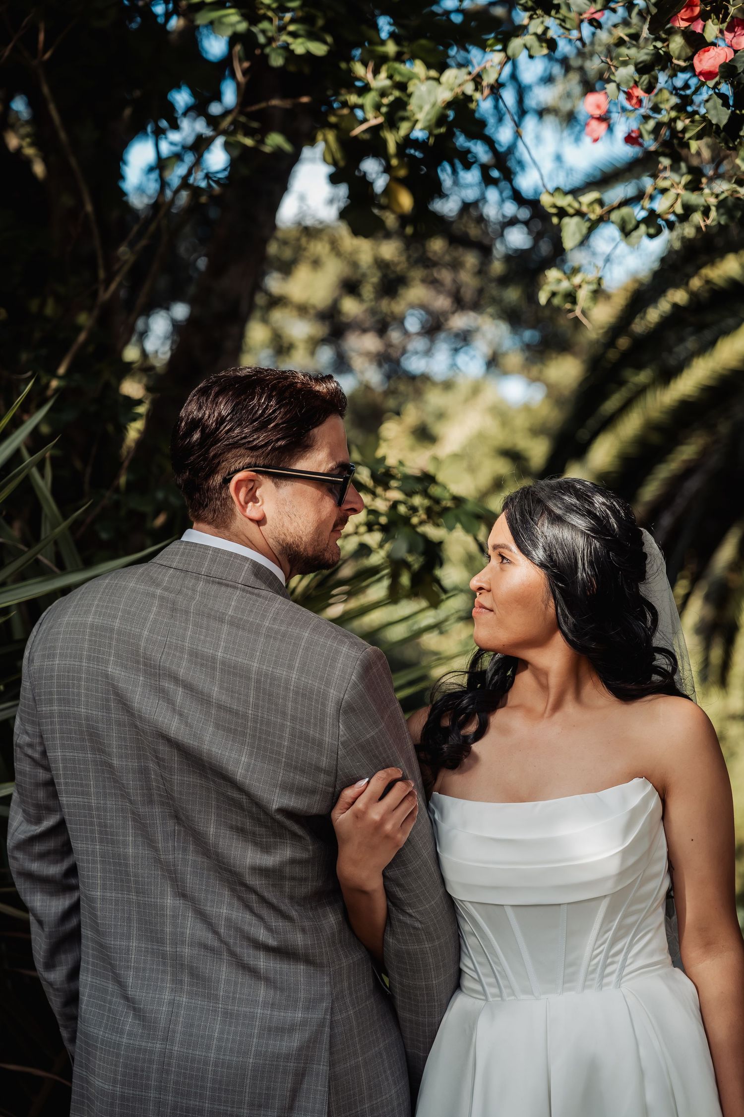 Bride and groom share a tender moment together beneath lush green trees at their outdoor wedding.
