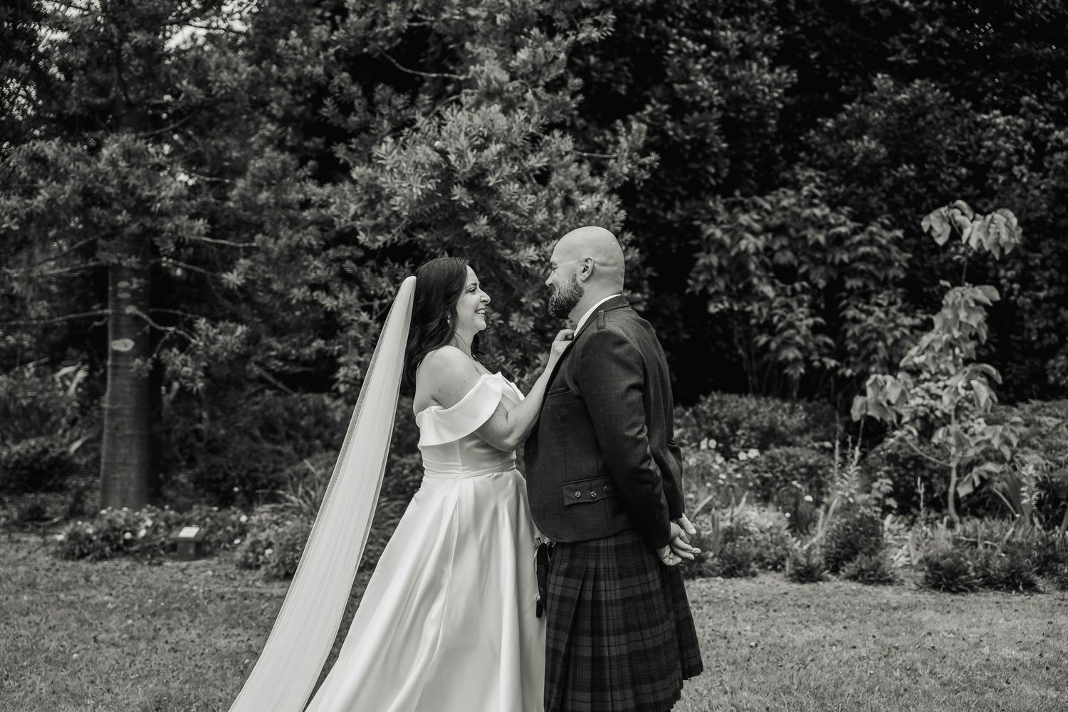 Black and white photo of bride and groom gazing at each other in a lush garden.