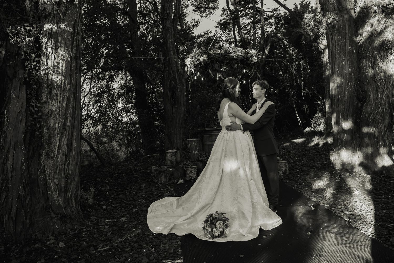 Black and white romantic portrait of bride and groom embracing in wooded garden setting.