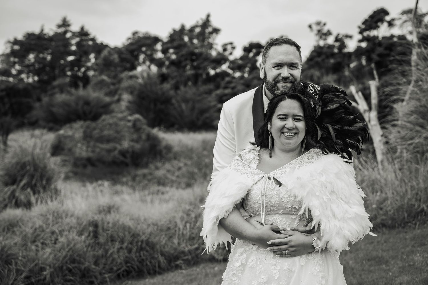 Black and white portrait of smiling newlywed couple embracing outdoors in natural landscape.