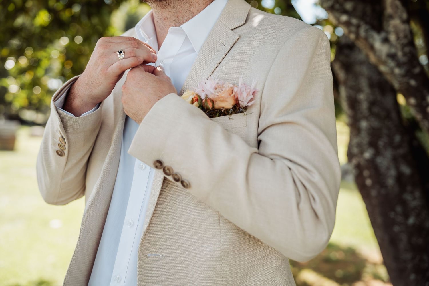Close-up of groom in beige suit adjusting boutonniere with floral pocket square.