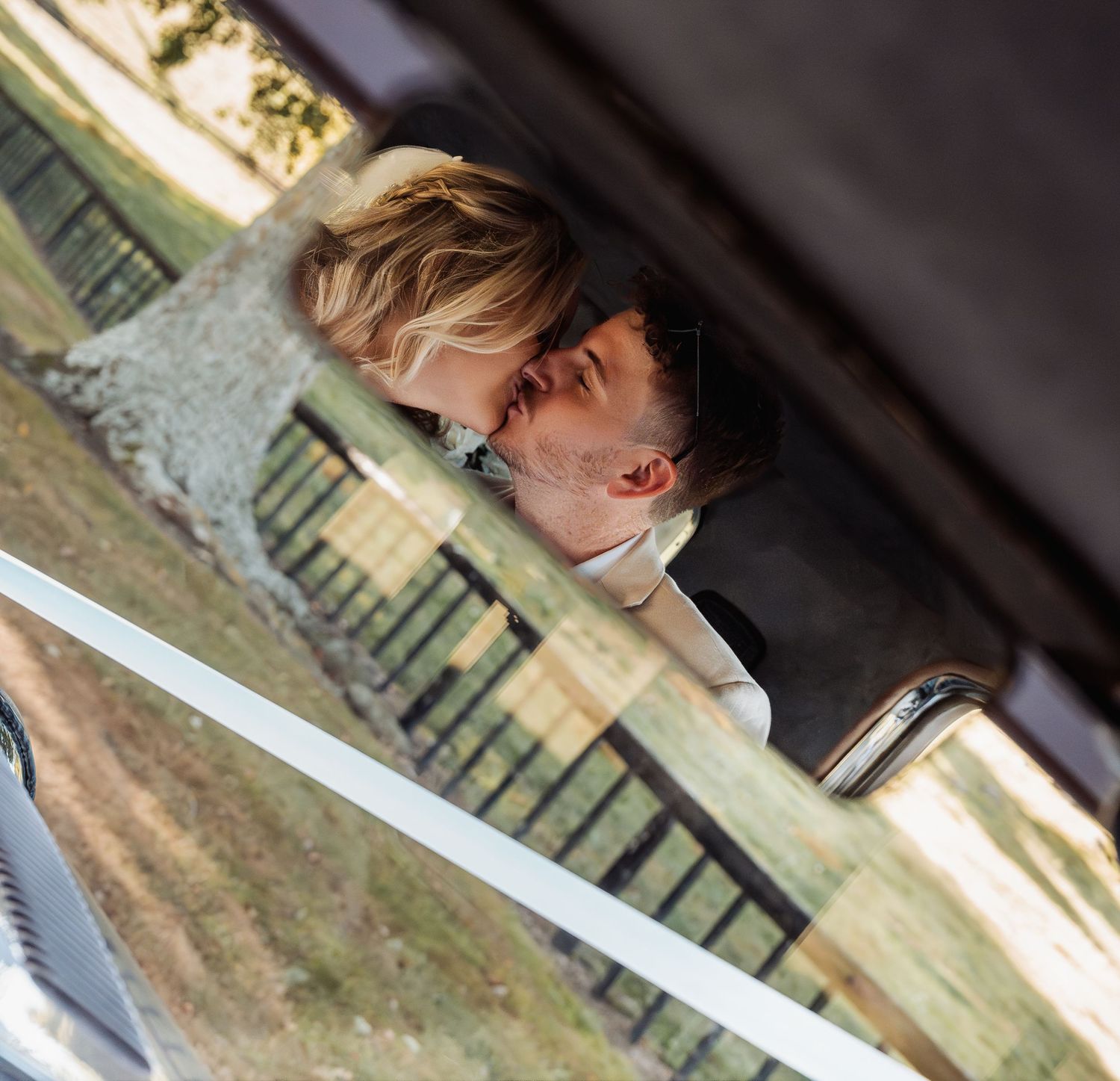Romantic bride and groom sharing a kiss captured through a vintage car window reflection.