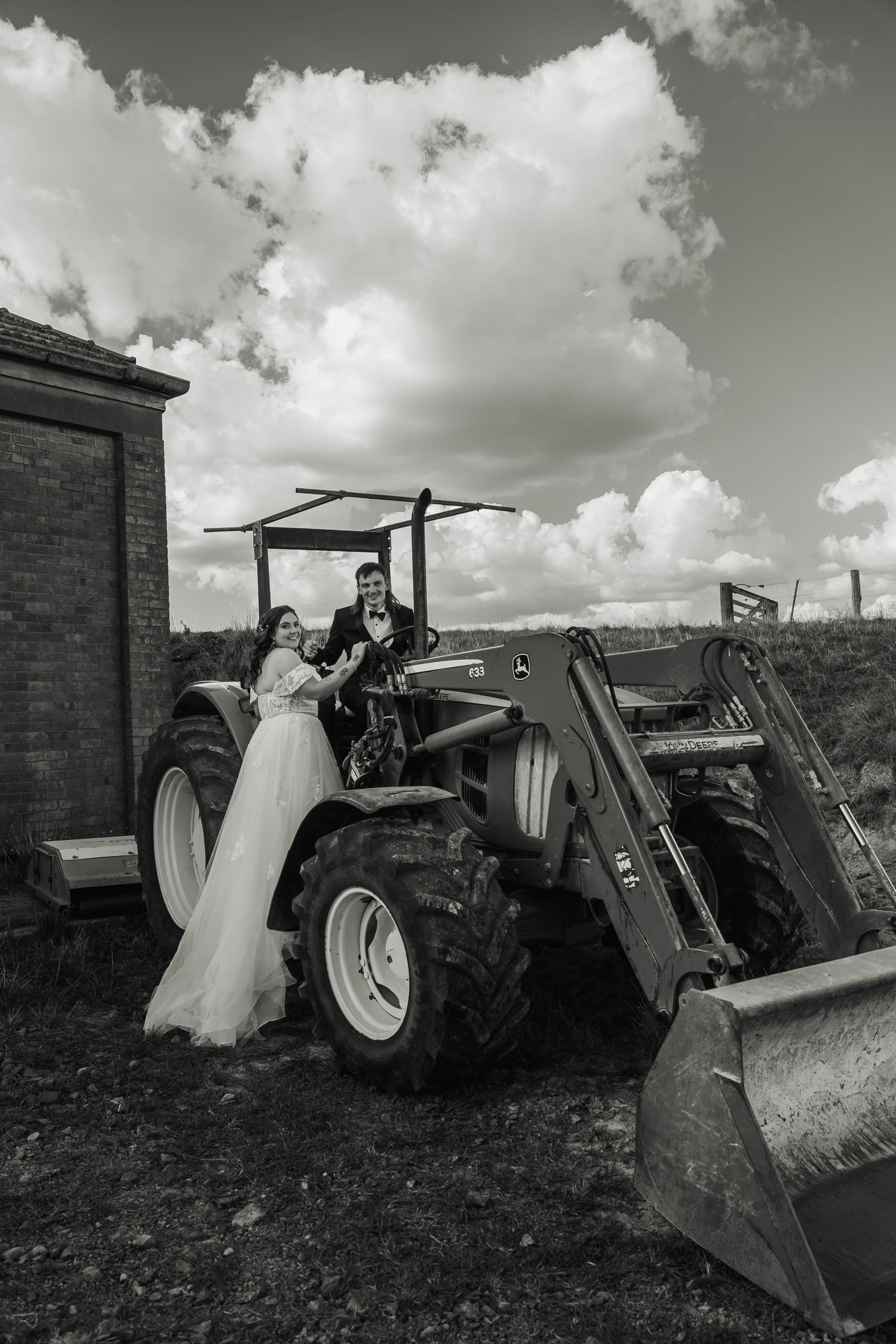 Bride and groom posing with a vintage tractor on their wedding day in black and white photo.