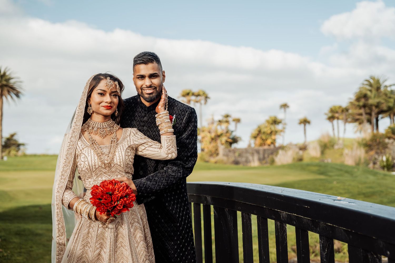 A couple poses for wedding photos on a golf course with palm trees and blue skies.