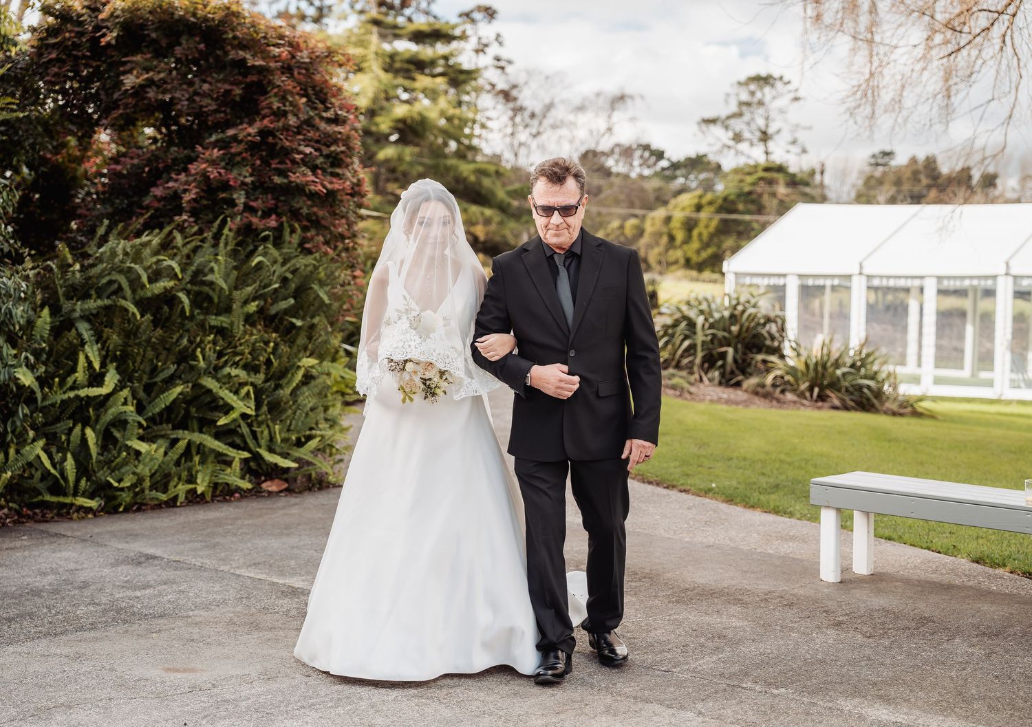 A wedding couple walks together through a garden path with elegant white accents and landscaping.