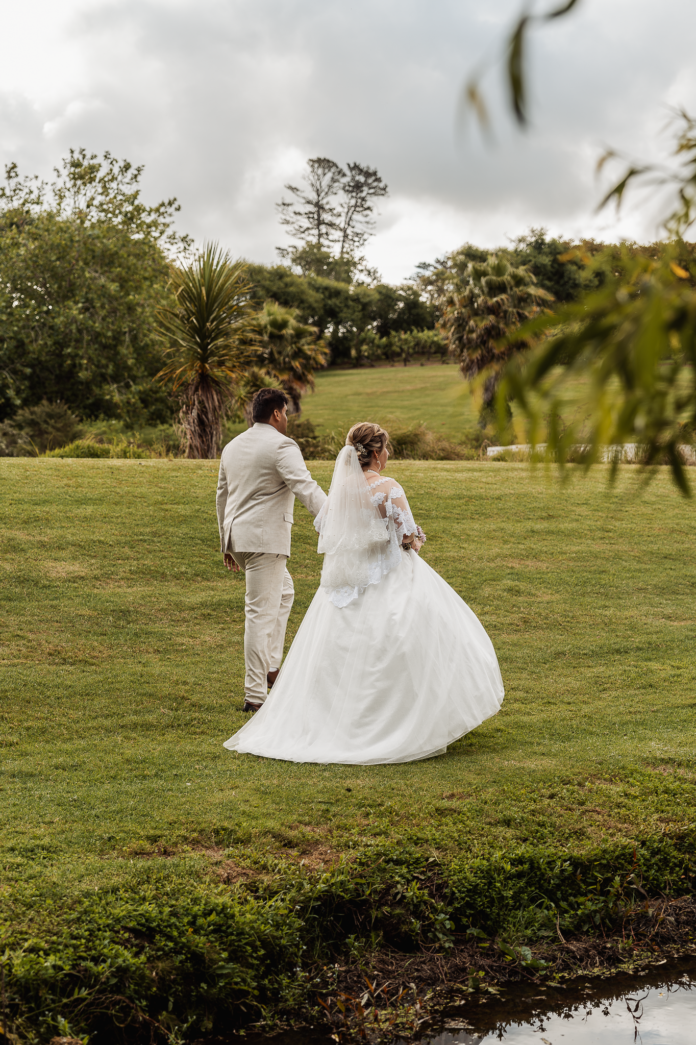 A wedding couple walks through a lush green garden setting on their special day.