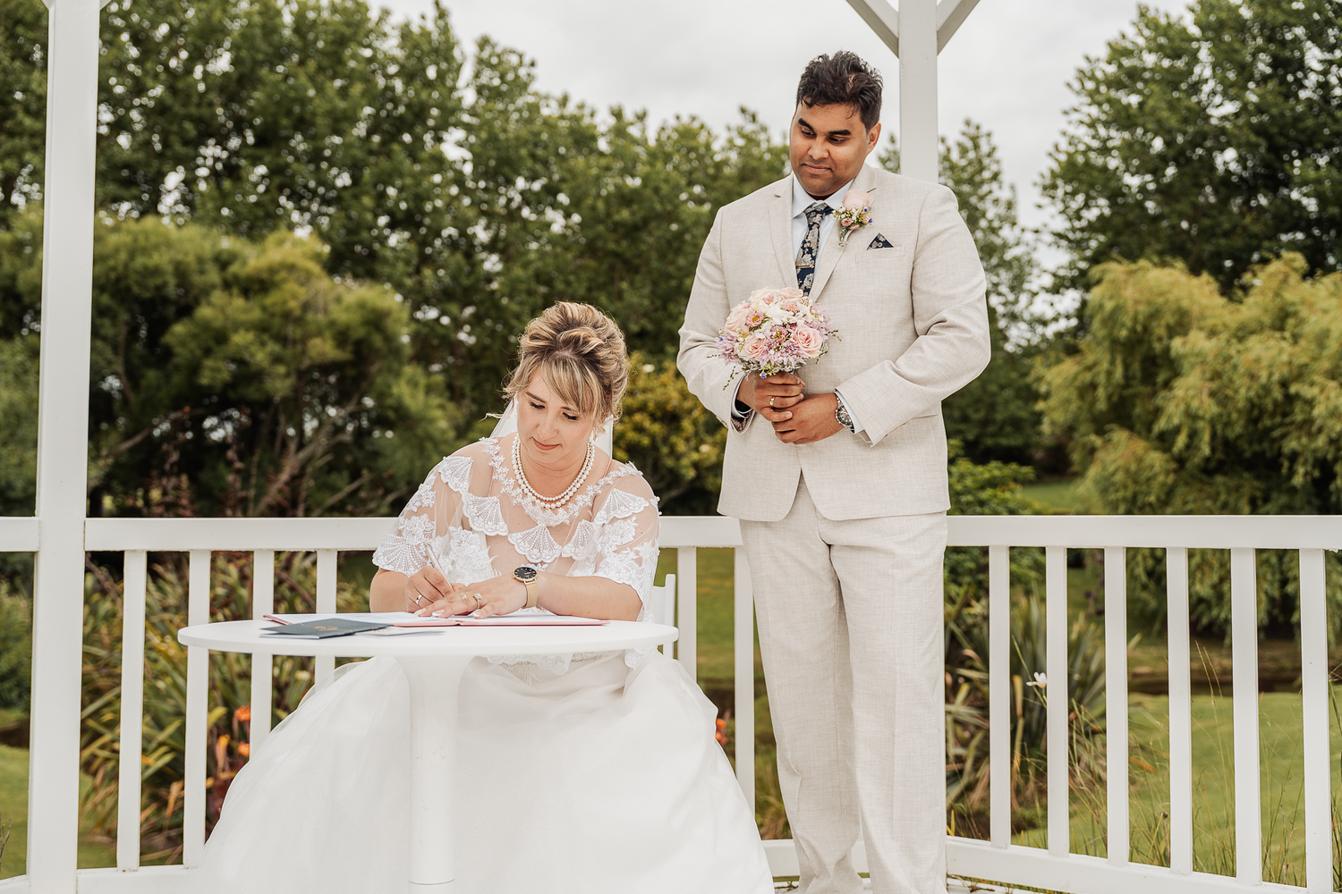 A couple signs documents during their outdoor wedding ceremony under a white gazebo.