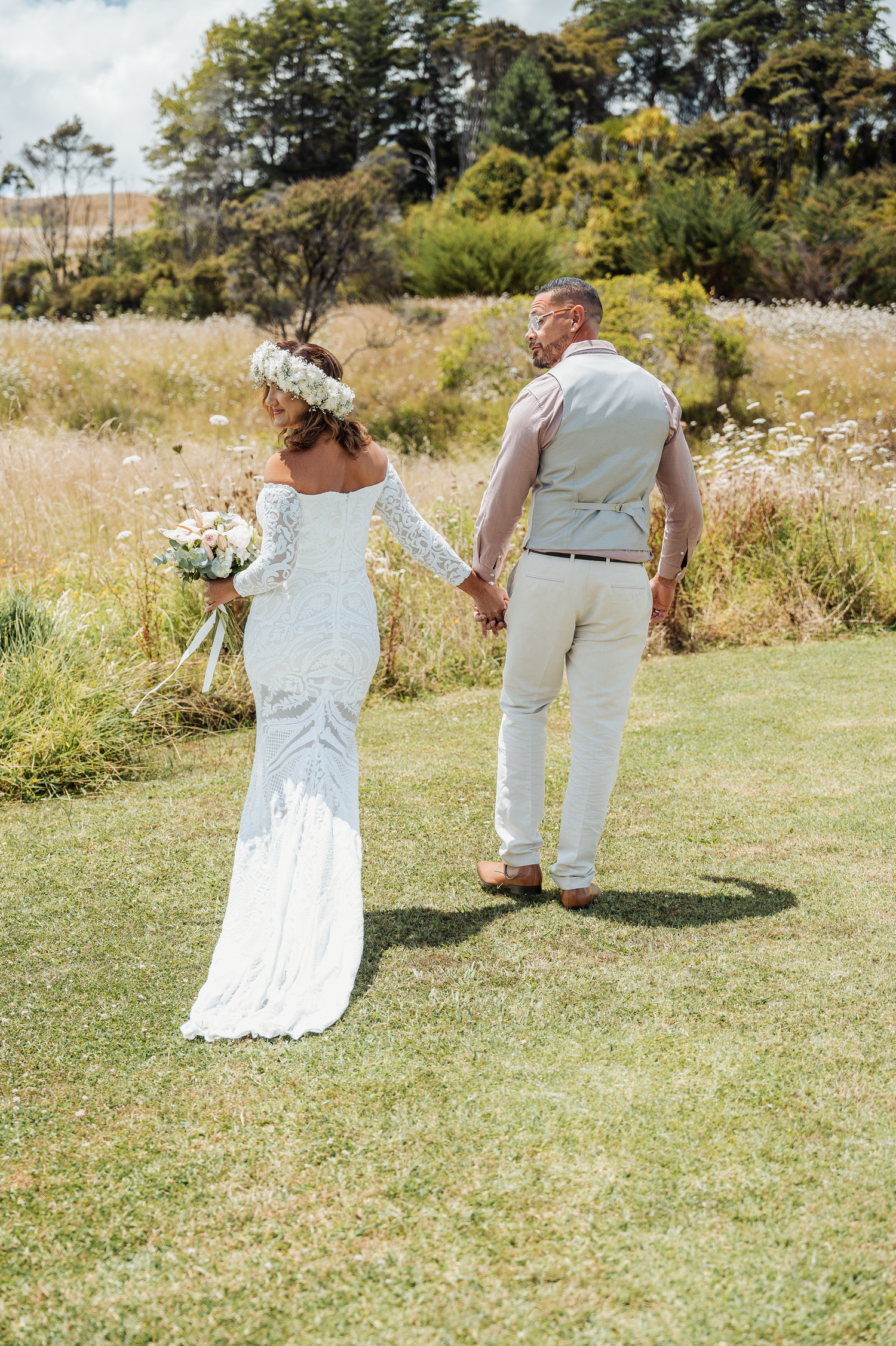 Wedding couple walking hand in hand through a scenic meadow on their special day.