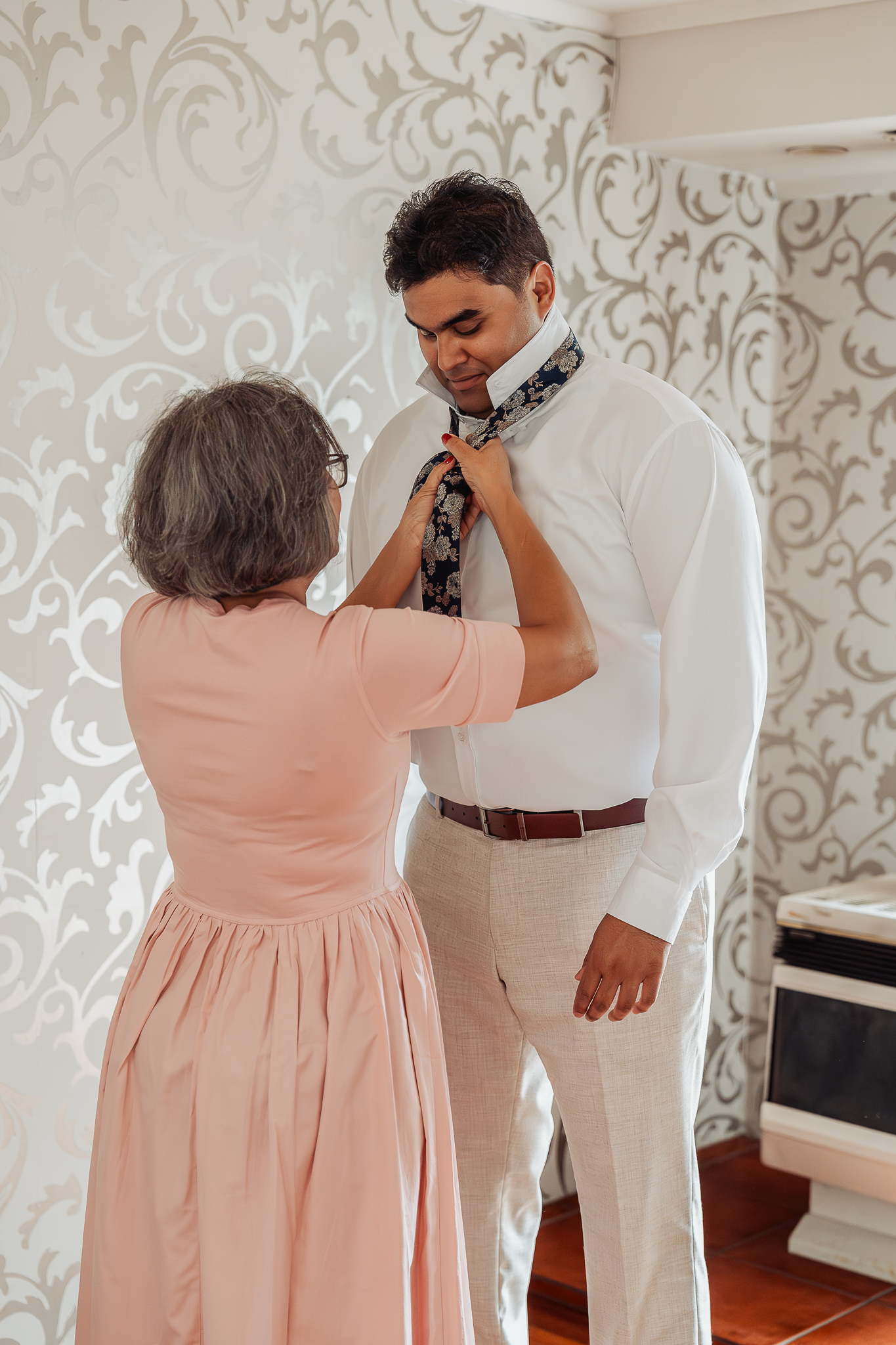 Someone helps adjust a tie on a person wearing white dress shirt.