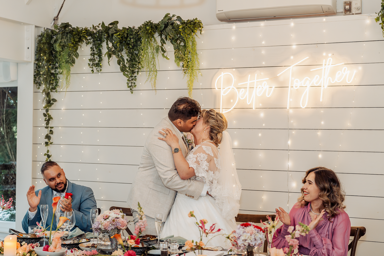 A couple shares a tender moment during their wedding reception with guests dining in the background.